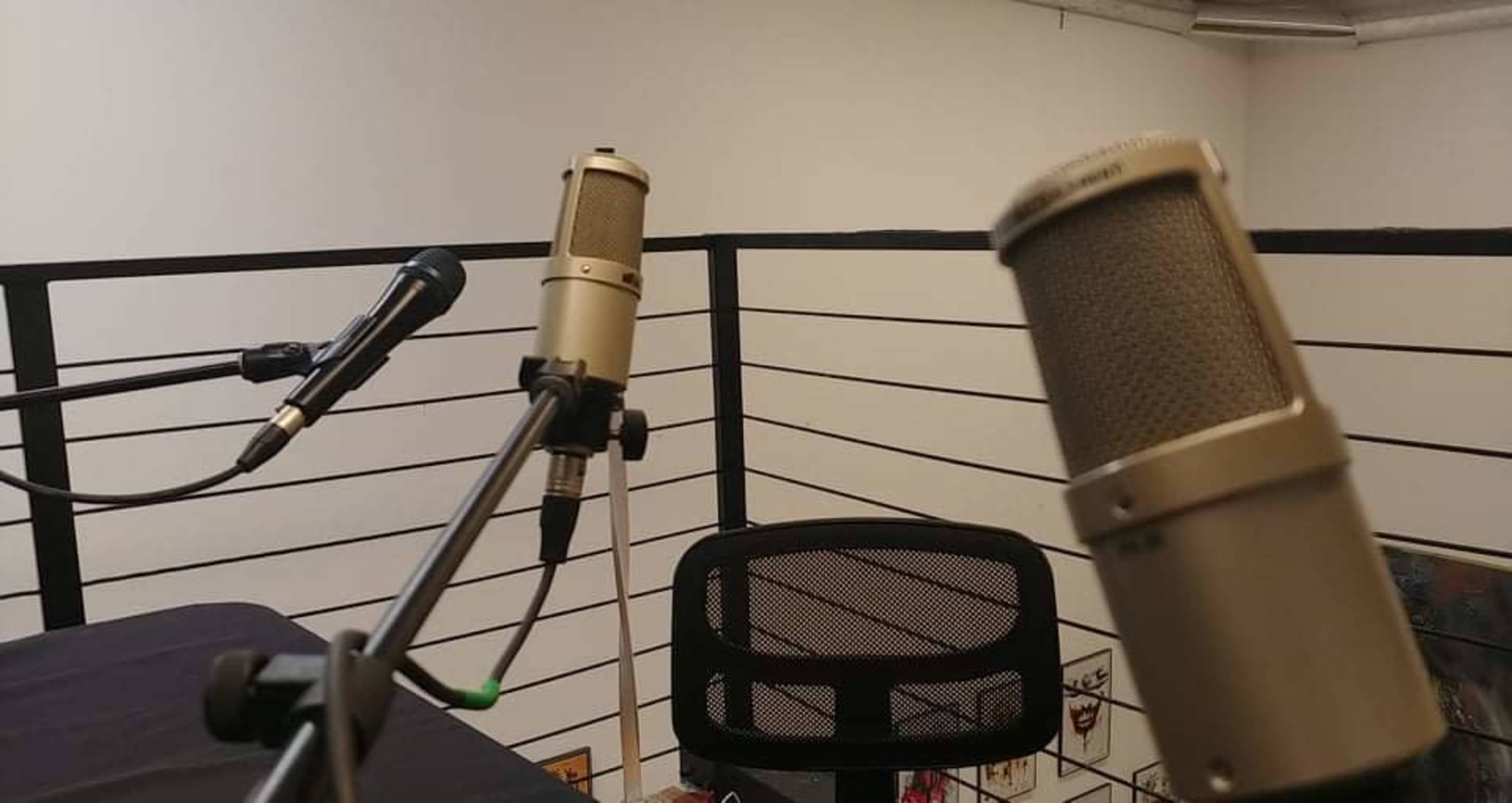 Two microphones are positioned on a table with a black tablecloth, overlooking a balcony area with a chair in a studio setting.