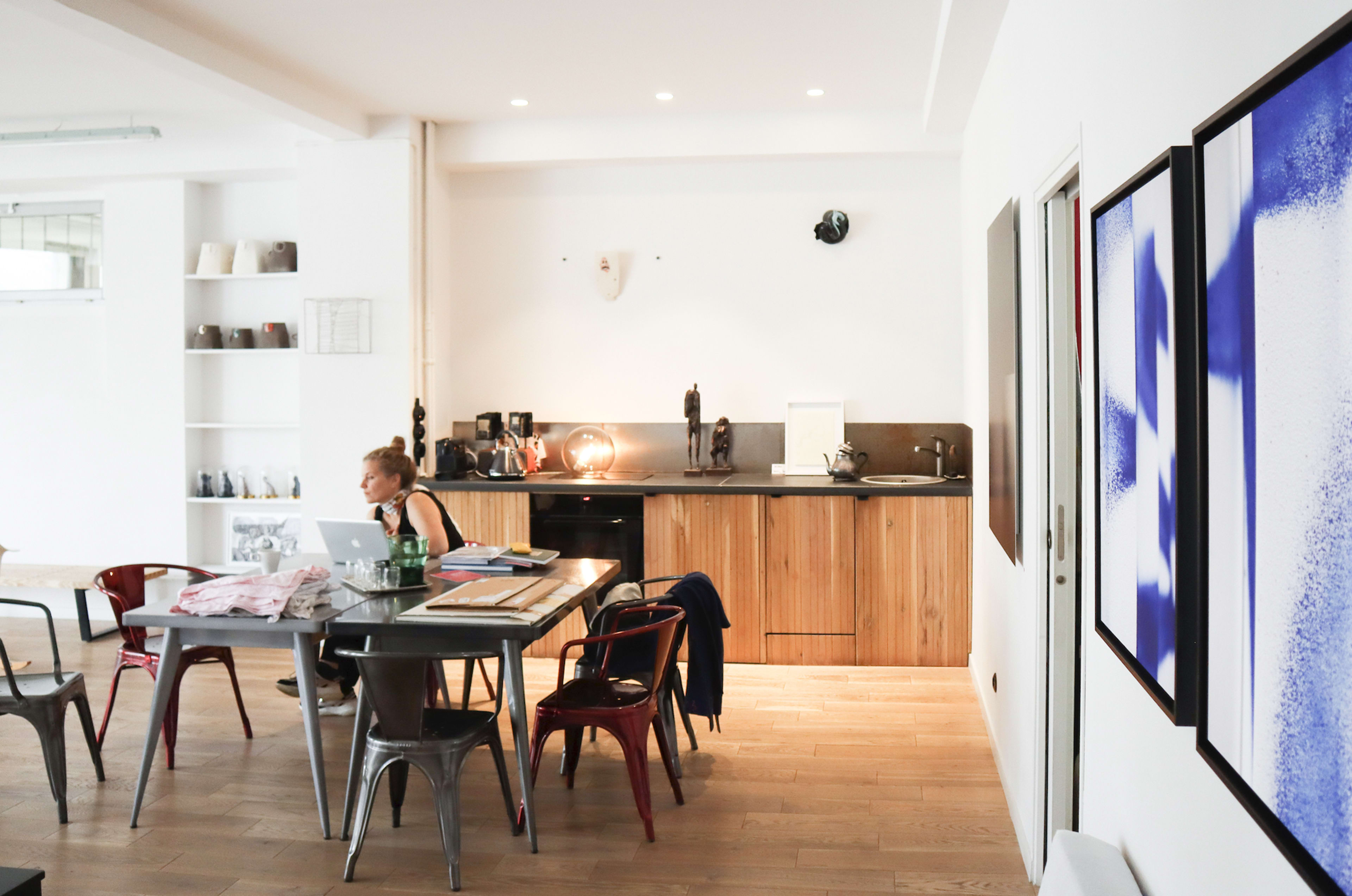 A person is sitting at a table with a laptop in a modern kitchen and dining area featuring wooden accents and framed artwork on the walls.