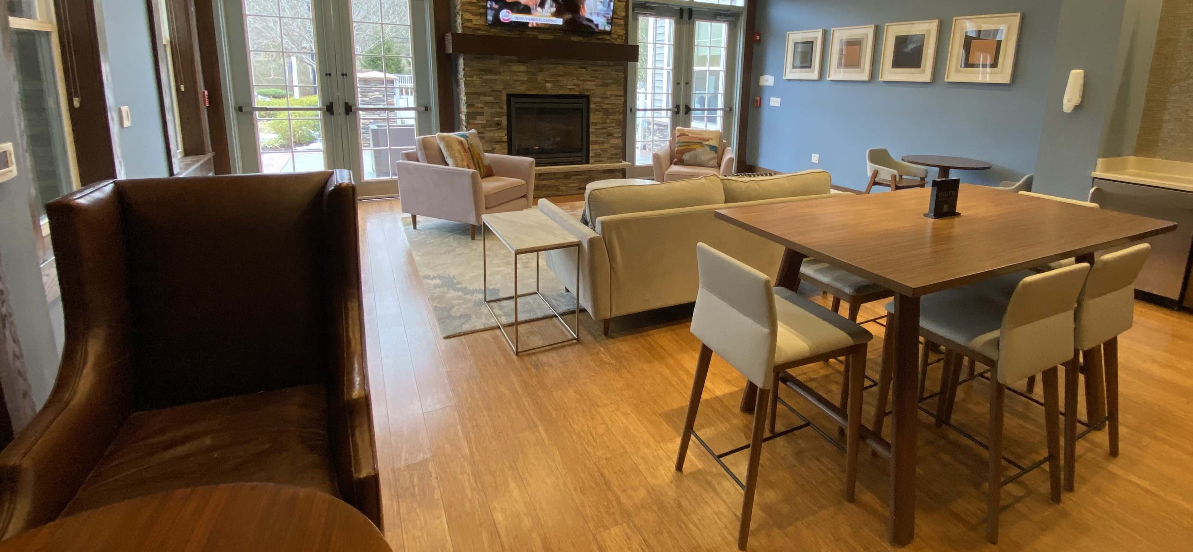A cozy lounge area featuring a fireplace, a dining table, and various seating arrangements, all set in a well-lit space with large windows.