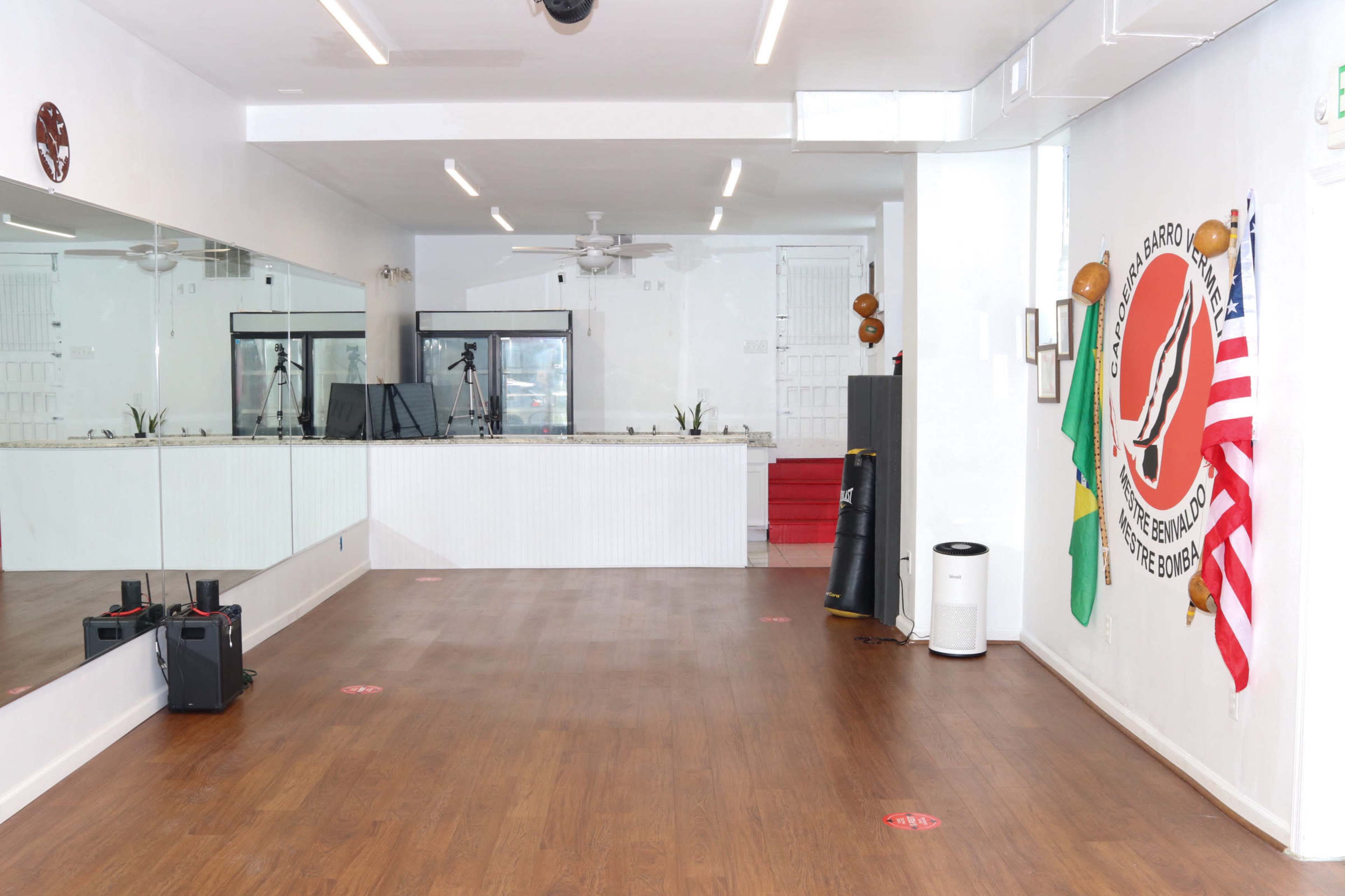 A spacious, well-lit room with wooden flooring, featuring a mirrored wall, flags, and exercise equipment in the corner.