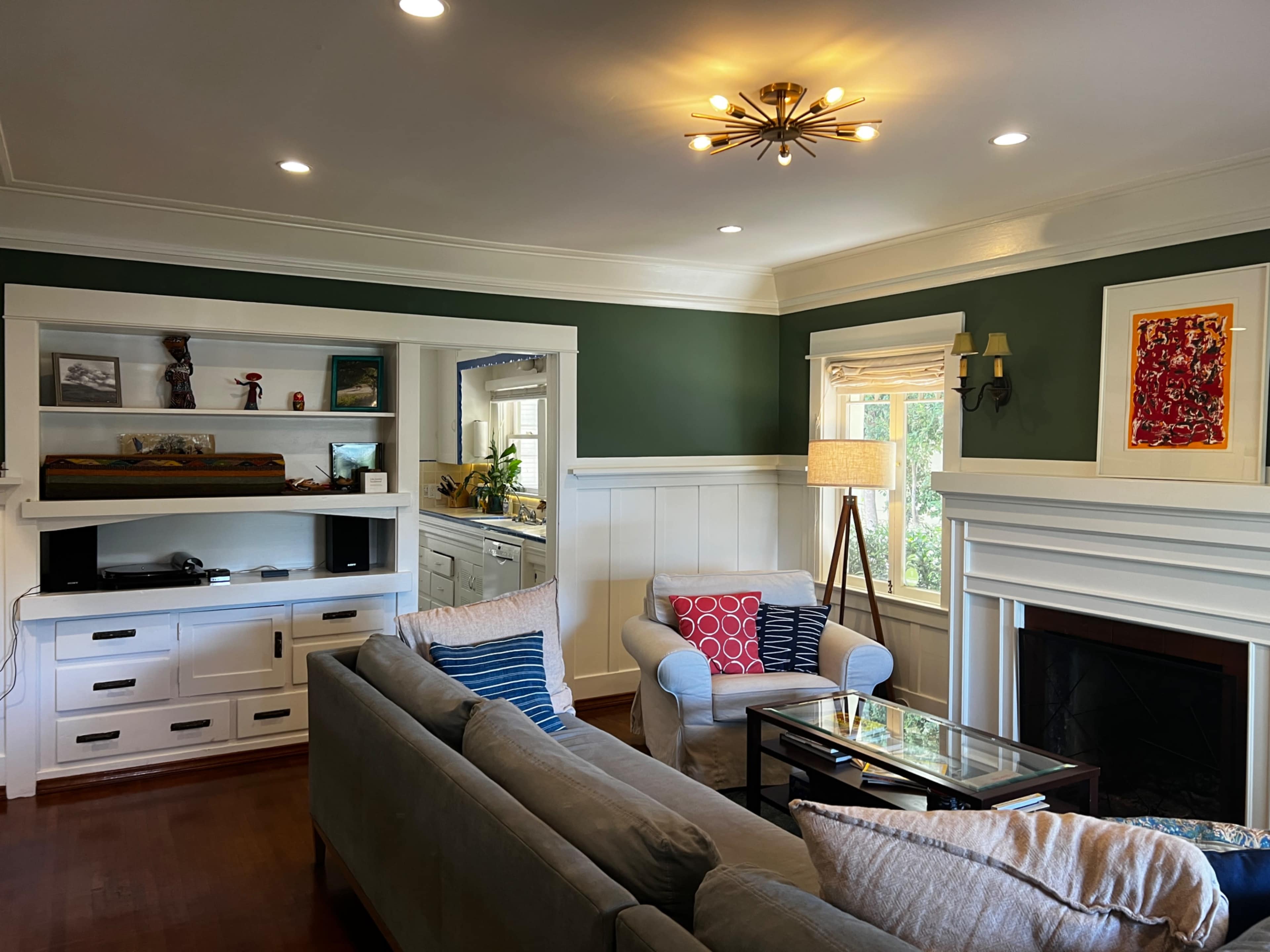 The image shows a cozy living room with a green accent wall, a comfortable gray sofa, and built-in shelving displaying decorative items.