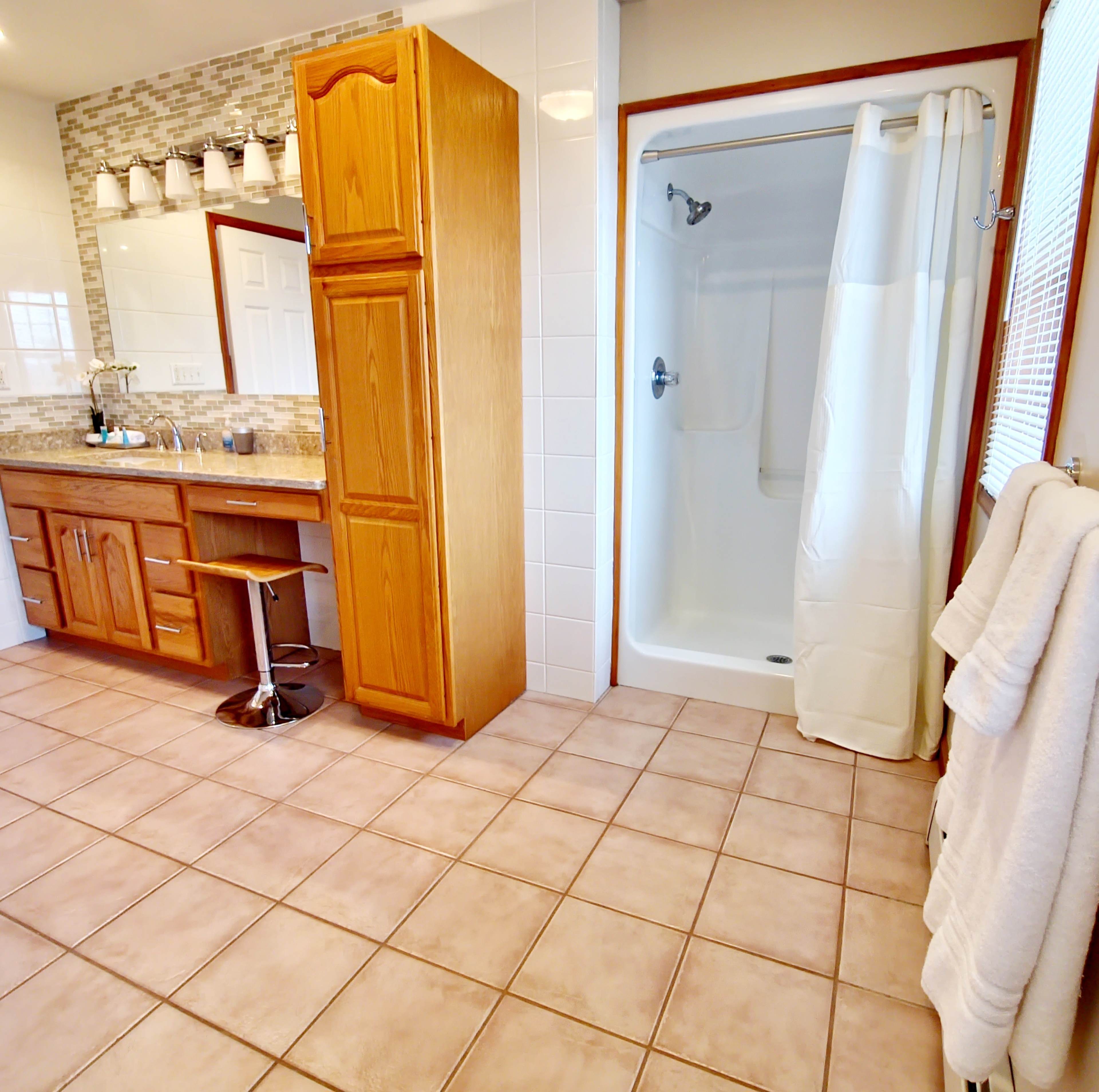 A spacious bathroom featuring wooden cabinetry, a large mirror, a shower area with a curtain, and tiled flooring.