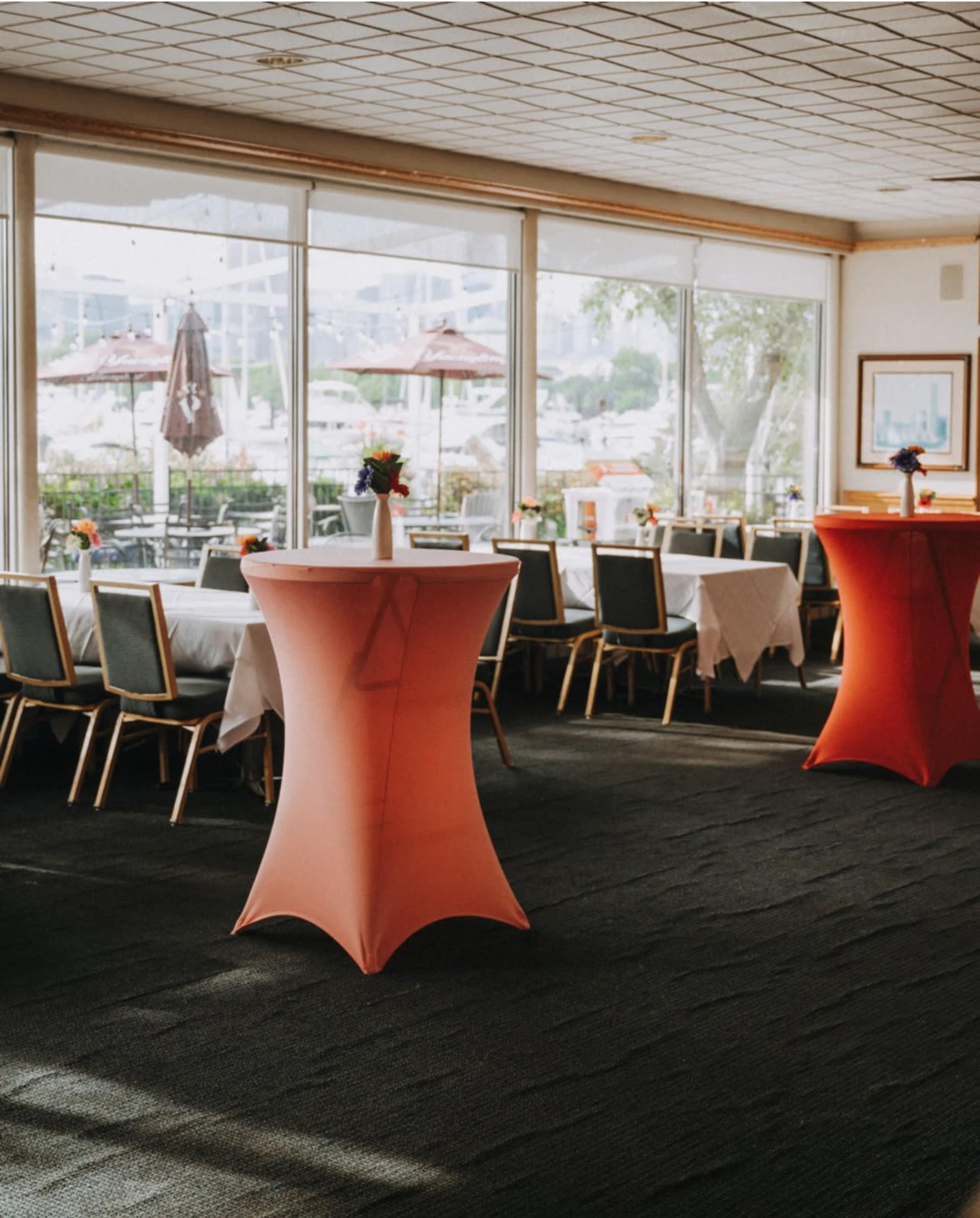 The image shows a restaurant interior with tables covered in white tablecloths and several orange cocktail tables.