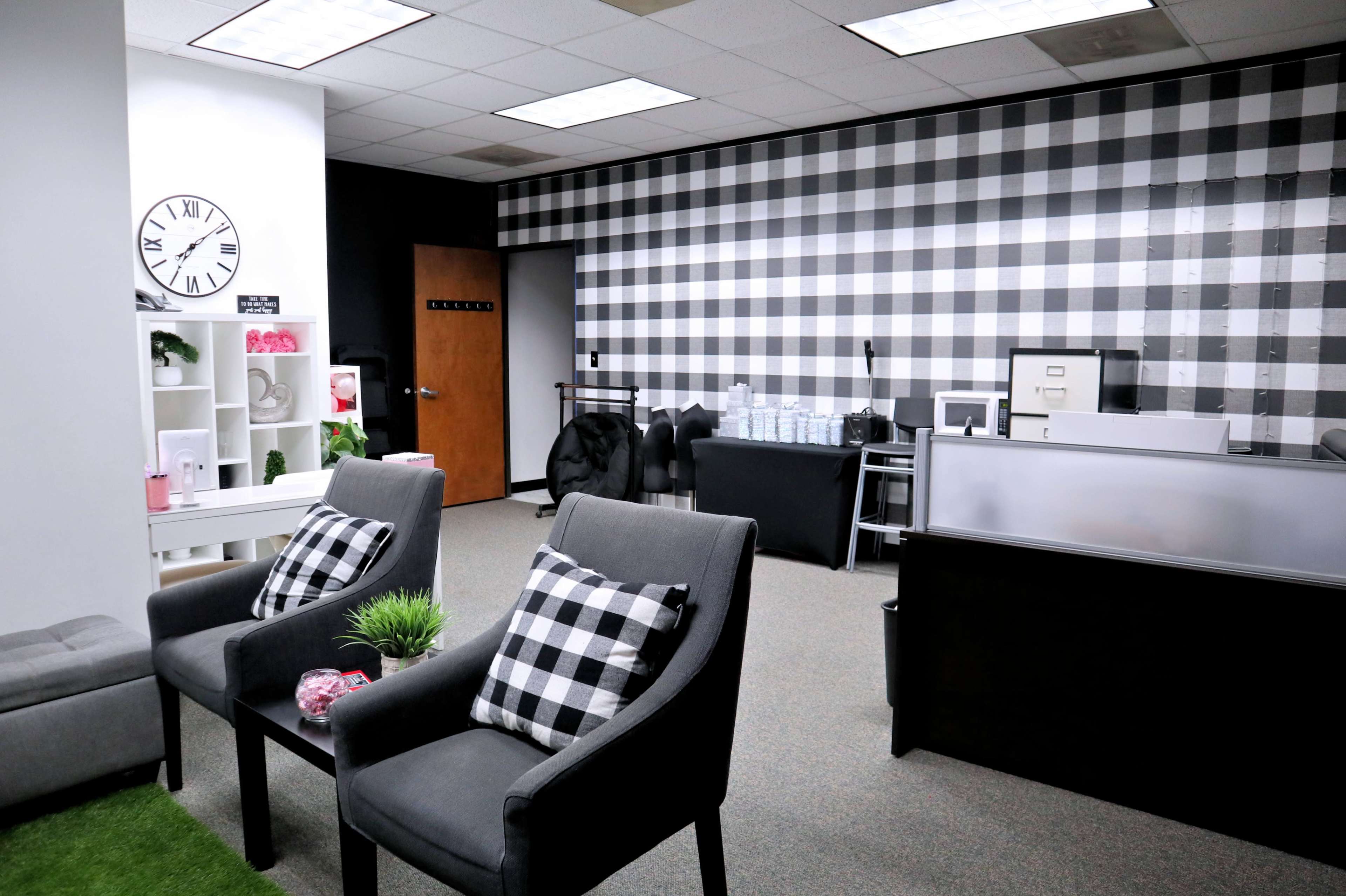 A modern office space with black and white checkered wall decor, two gray chairs with checkered cushions, and a reception area featuring a desk and storage cabinets.