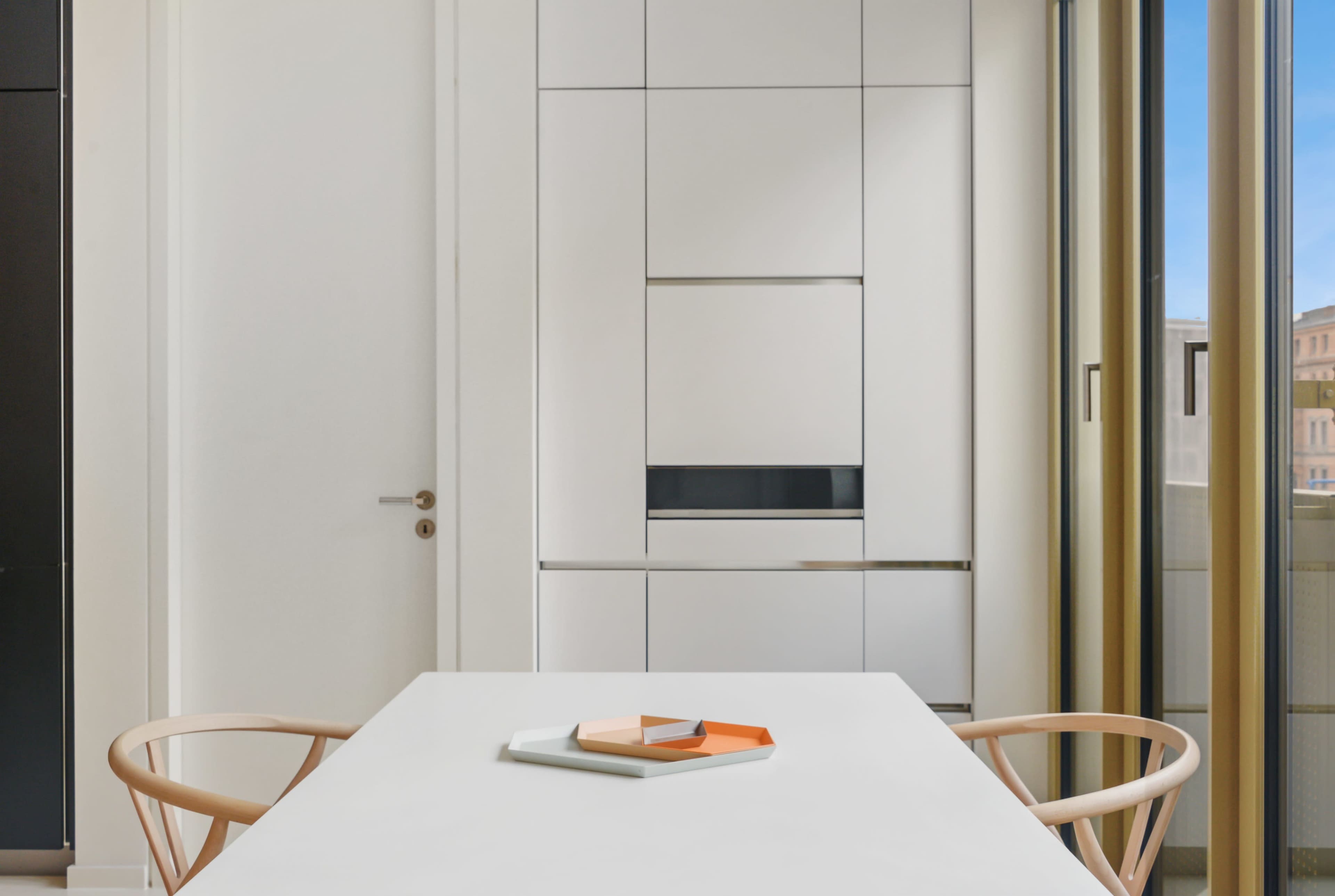 A minimalistic dining area features a white table with placemats and a wall cabinet in a bright, modern interior.
