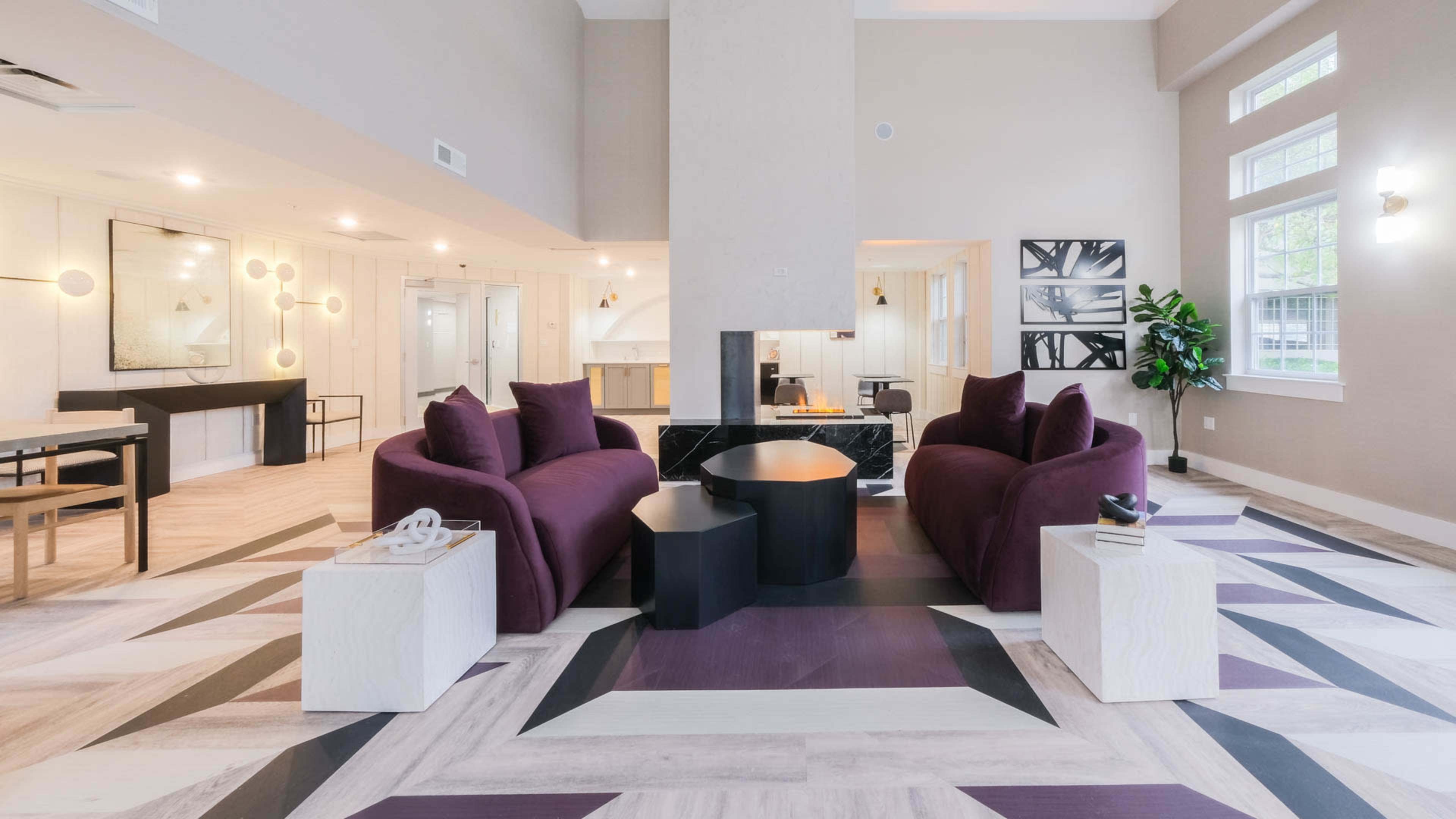 A modern lounge area featuring two purple sofas, a round coffee table, and a geometric patterned floor.