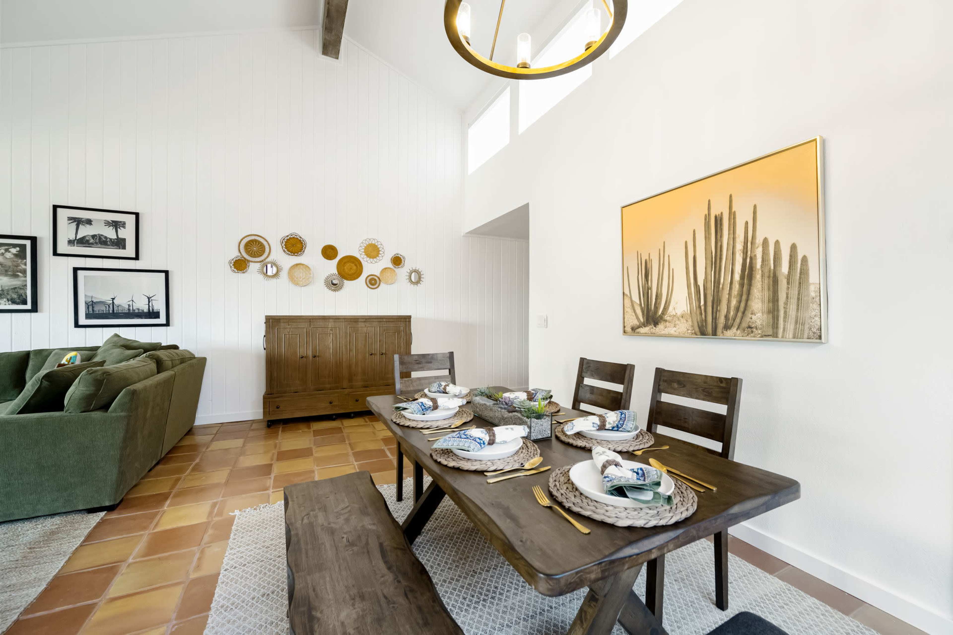A dining area features a wooden table set with plates and utensils, surrounded by a green sofa and adorned with wall art and decor.