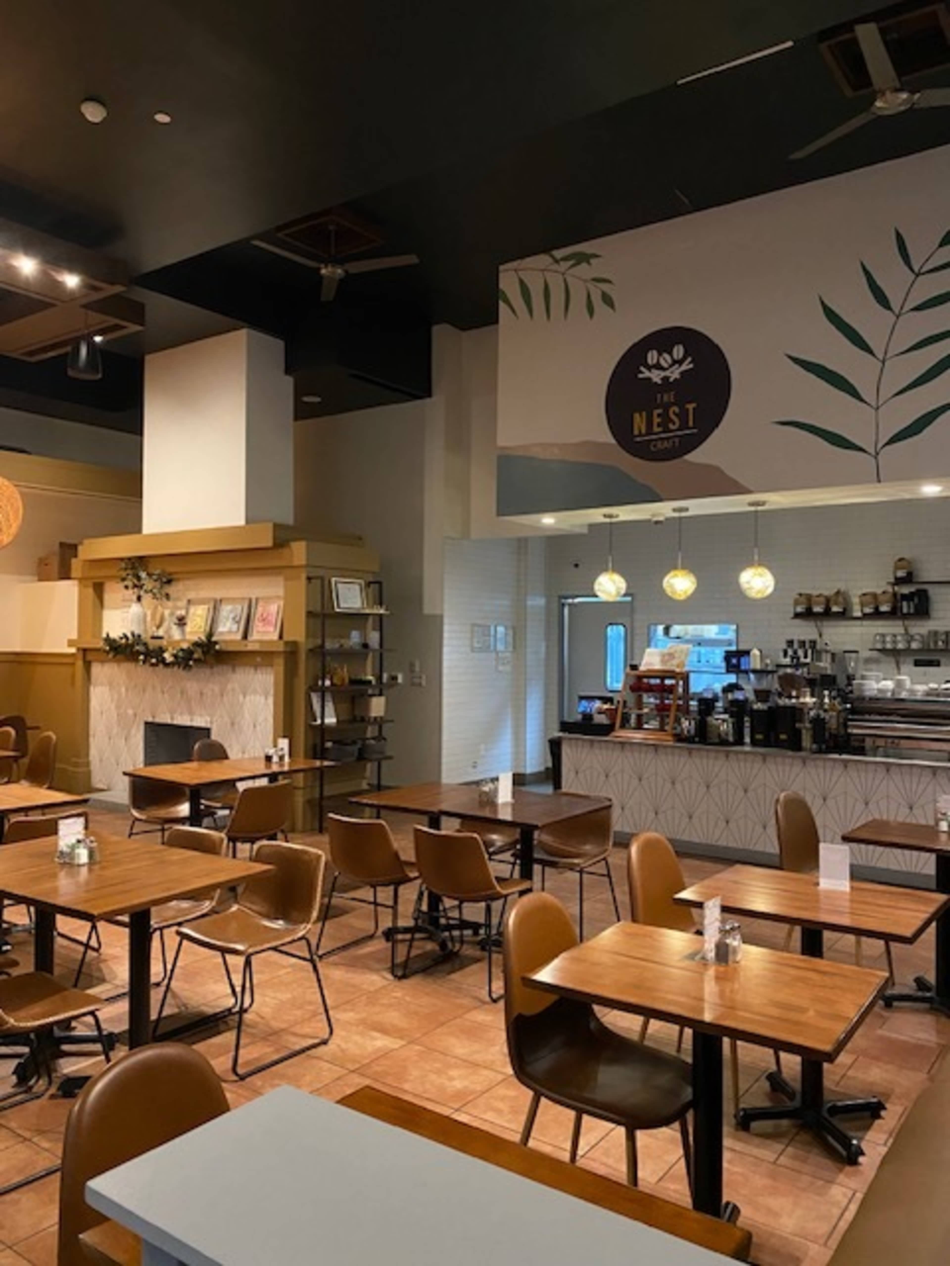 The image shows an interior of a cafe with wooden tables, brown chairs, and a counter displaying various food and drink items.