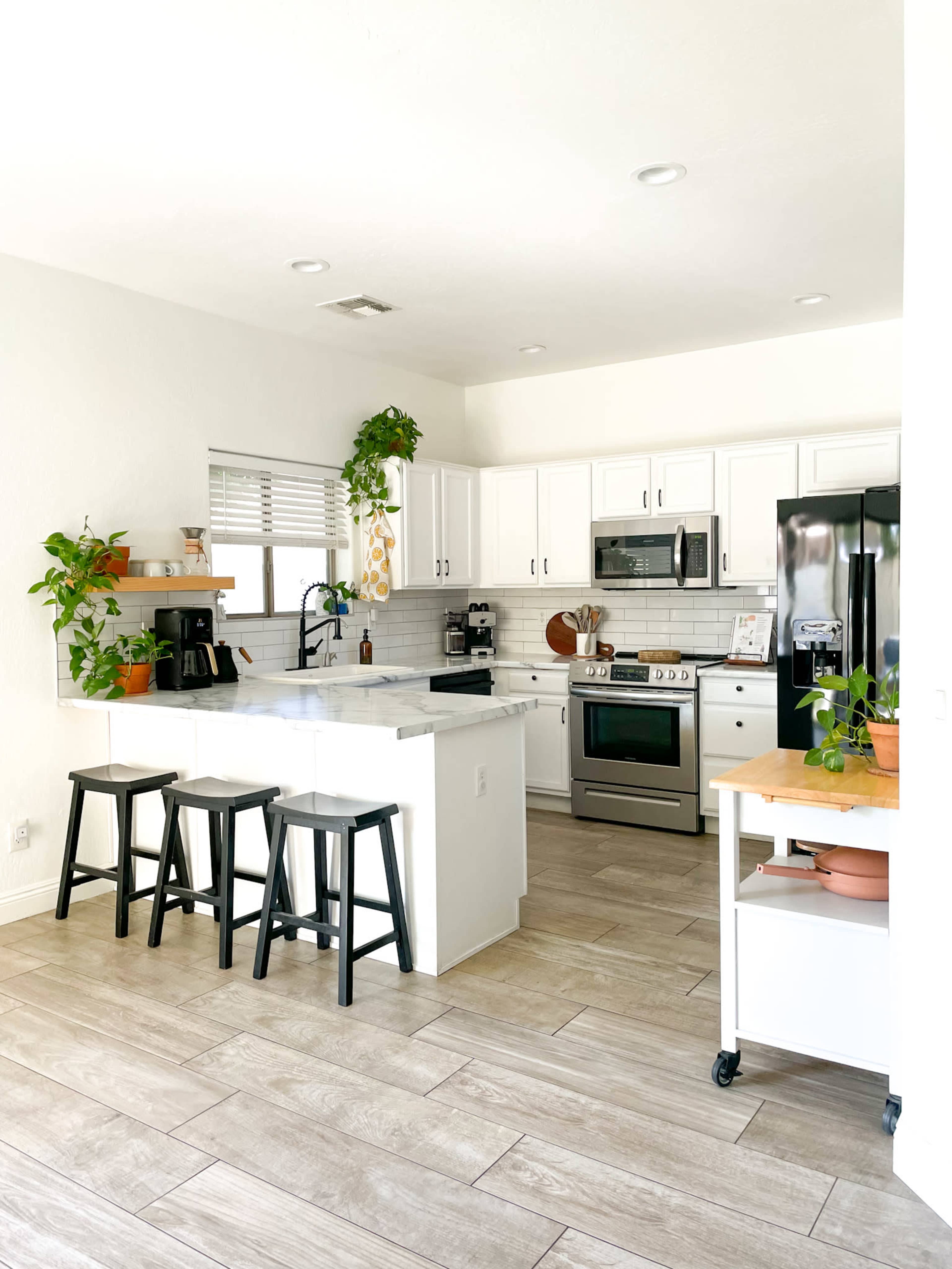 A modern kitchen with white cabinets, stainless steel appliances, and a wooden island with three black stools.