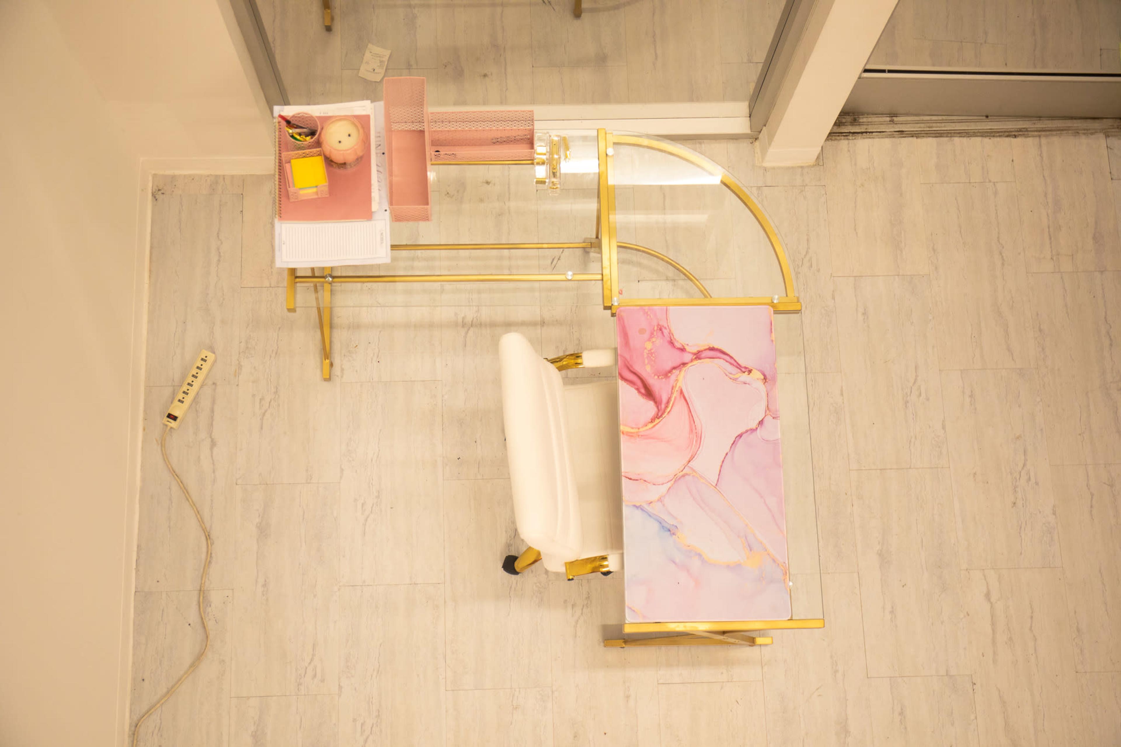 The image shows a modern desk with a pink and gold design, accompanied by a white chair and a neatly arranged workspace.