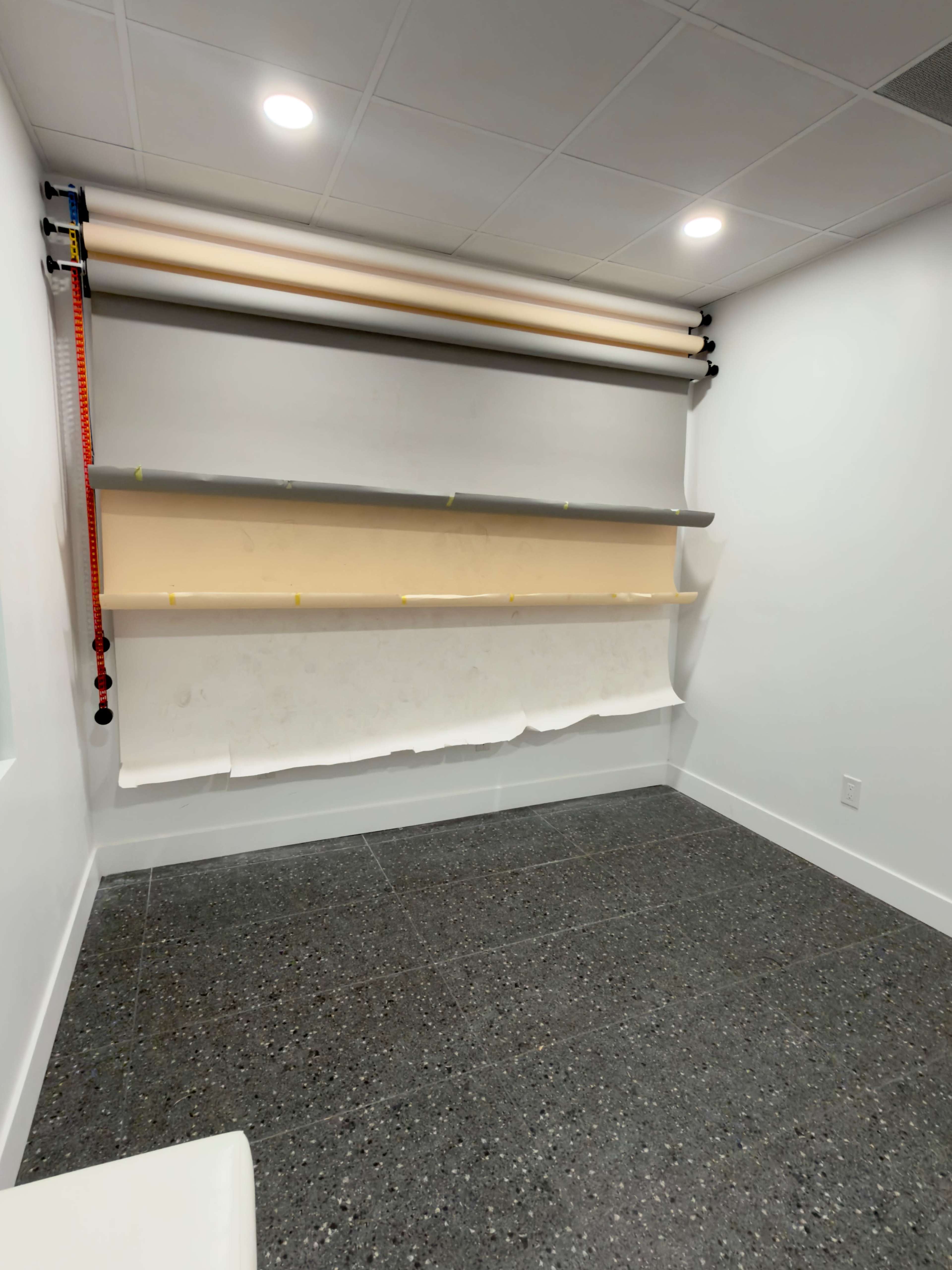 The image shows a well-lit room with a smooth, dark floor and a wall equipped with several rolls of paper and shelves for display or storage.