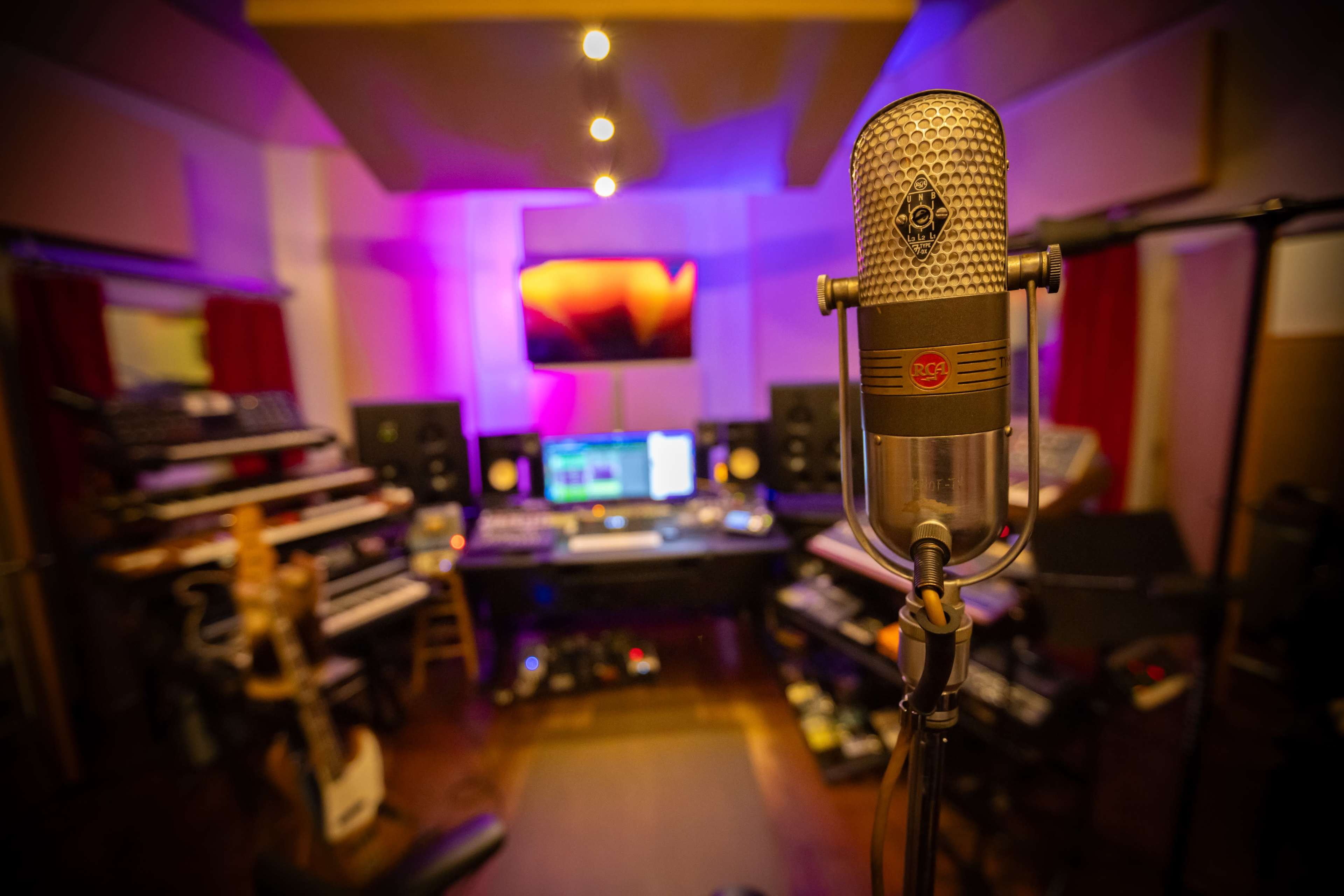 The image shows a recording studio with a microphone in the foreground and various musical instruments and equipment in the background.