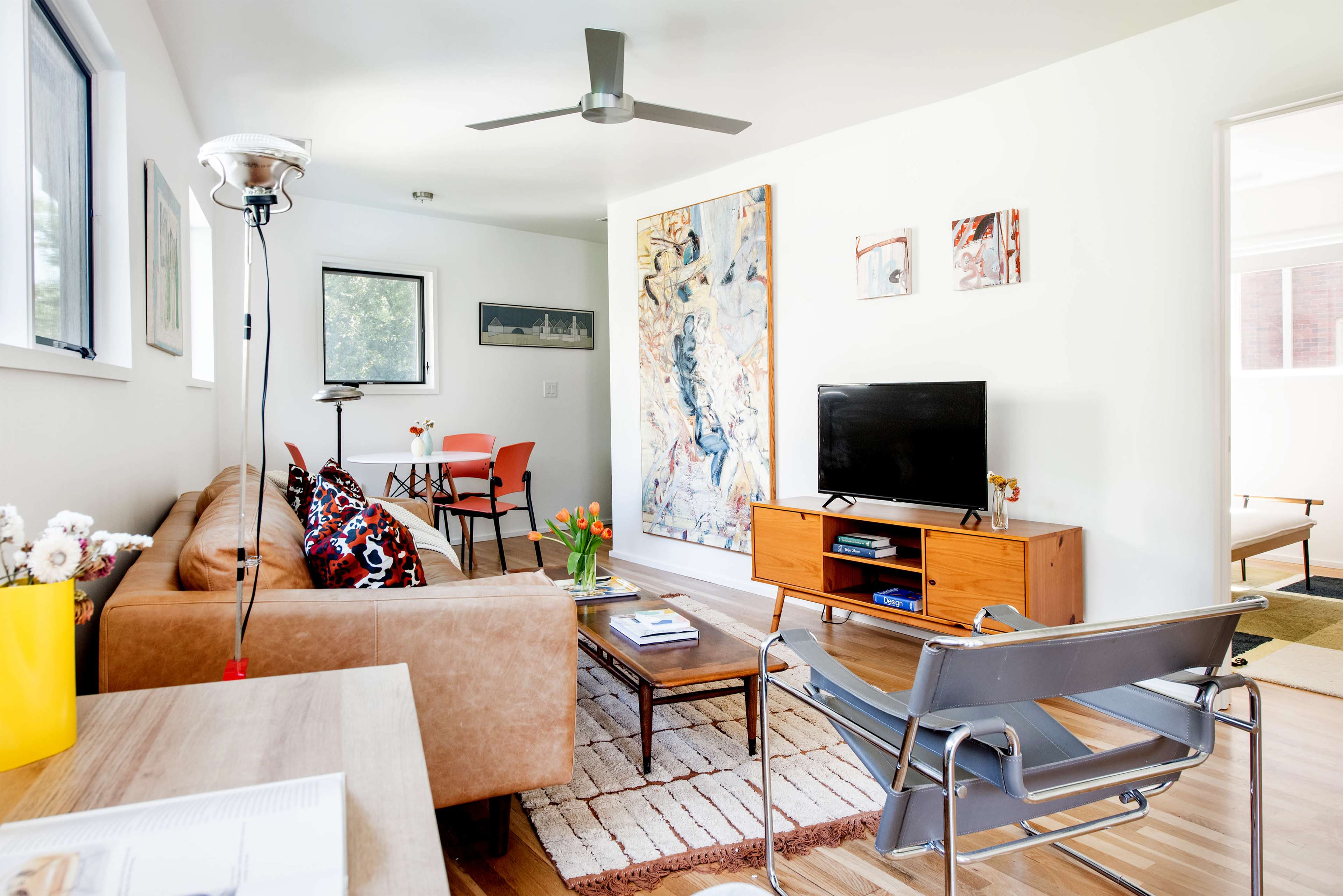 The image shows a modern living room featuring a brown couch, a coffee table, a television stand with a TV, and colorful artwork on the walls.