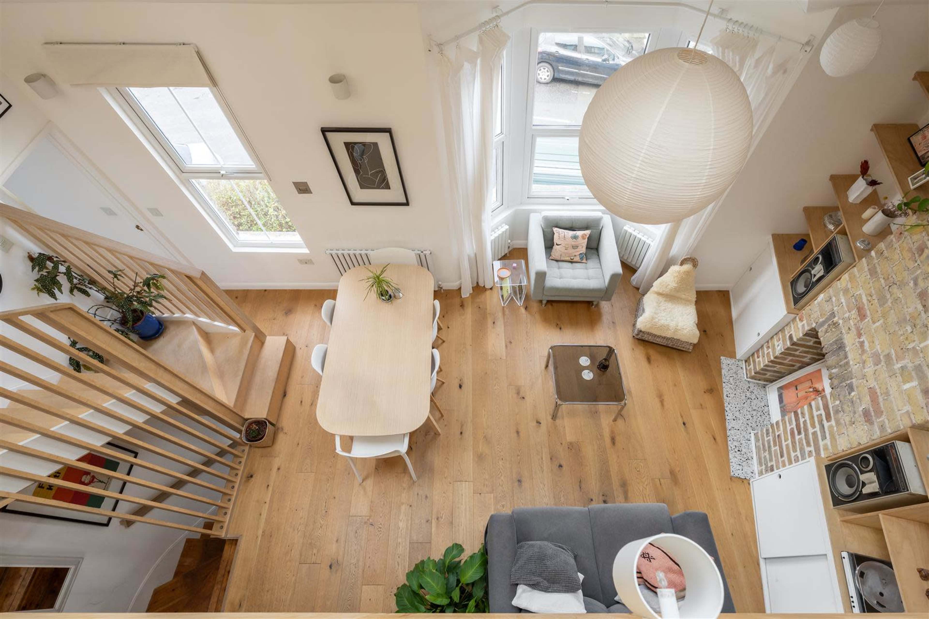 The image shows a bright and modern living area with a dining table, a seating area, and a staircase leading to an upper level.
