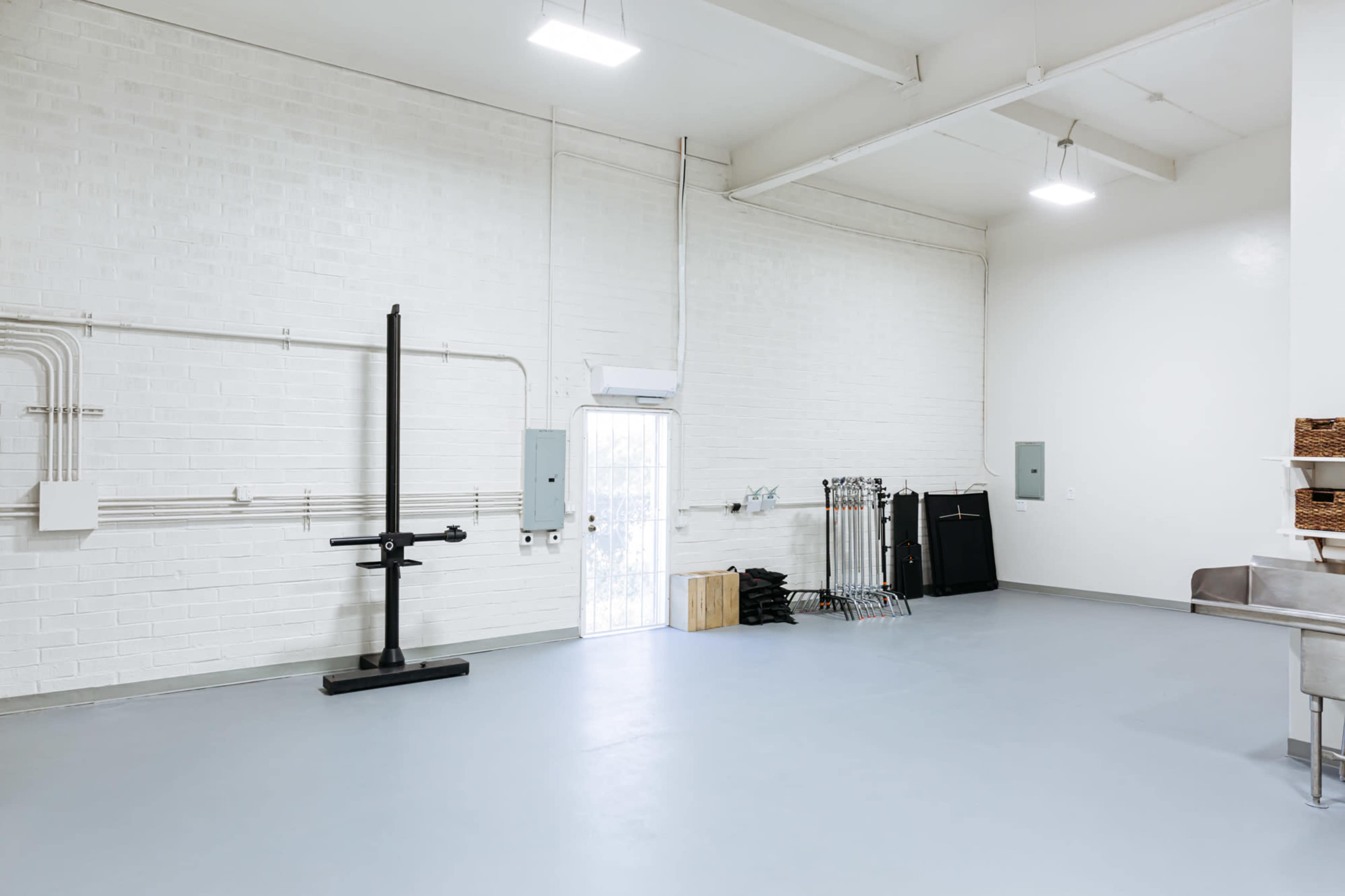 A spacious, empty interior of a room with white brick walls, a light grey floor, and minimal equipment along the sides.