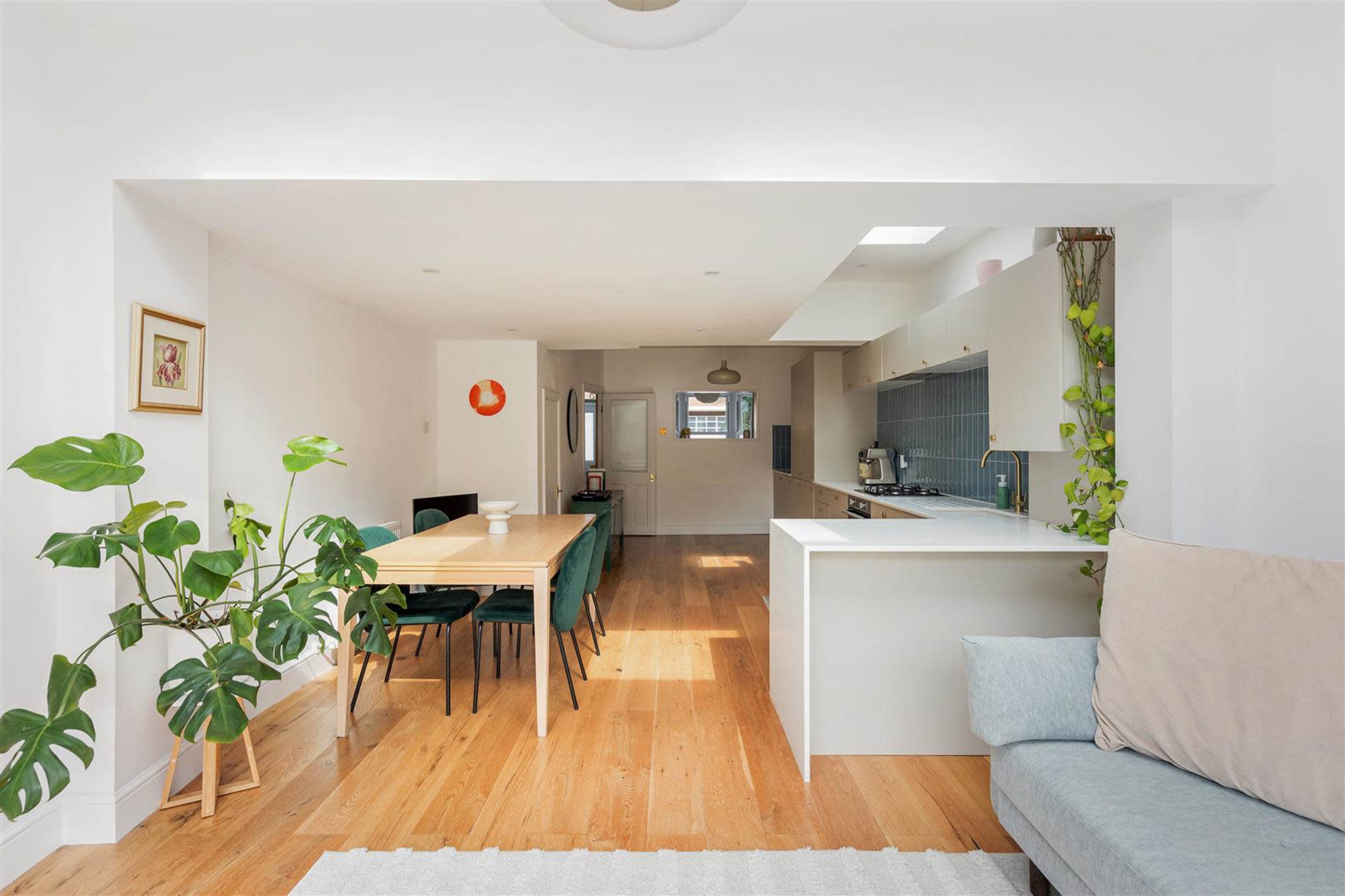 The image shows a modern, open-concept kitchen and dining area featuring a long wooden table, green chairs, and ample natural light.