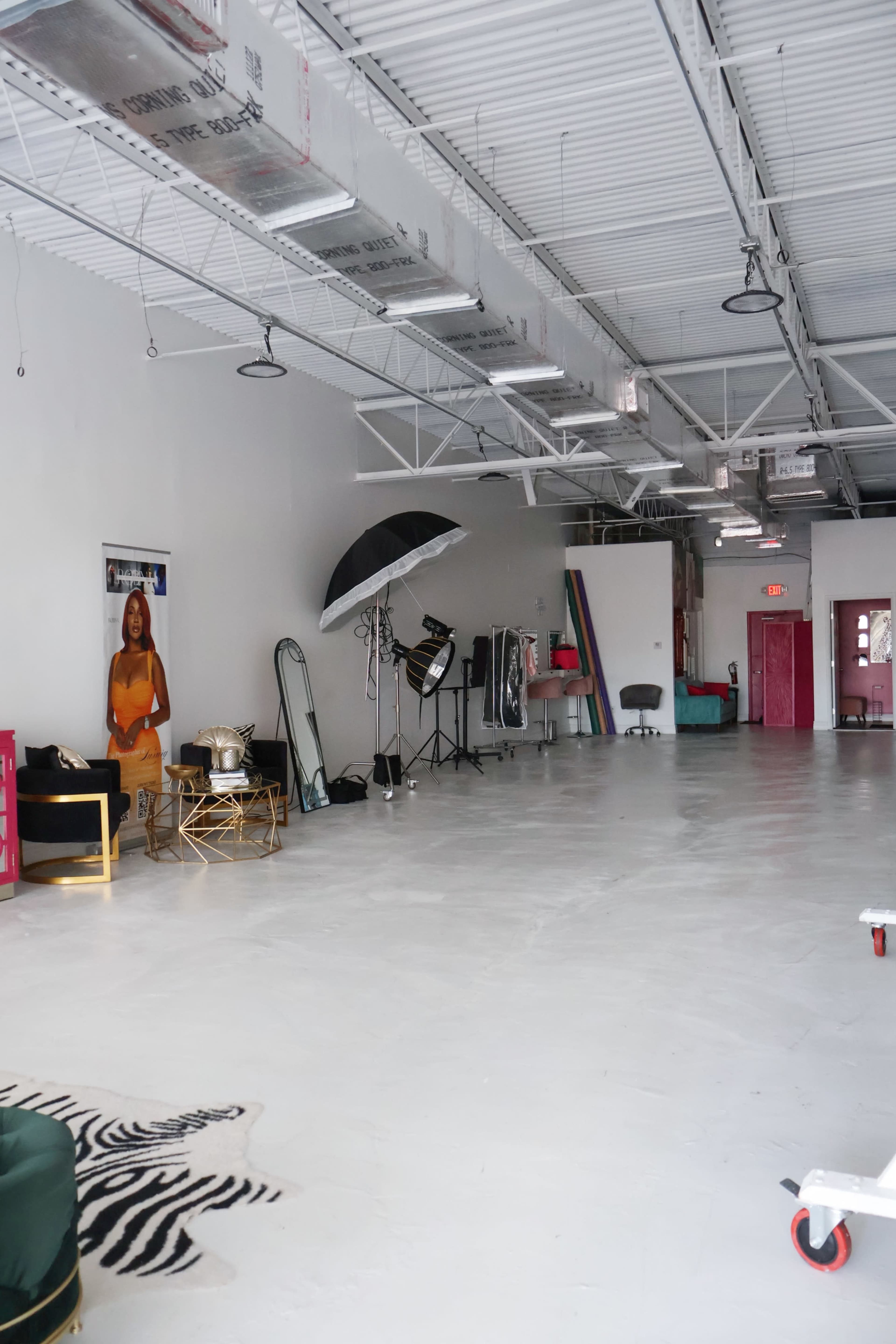The image shows an empty studio space with white walls, a concrete floor, and various photography equipment scattered around, including lights and a backdrop stand.