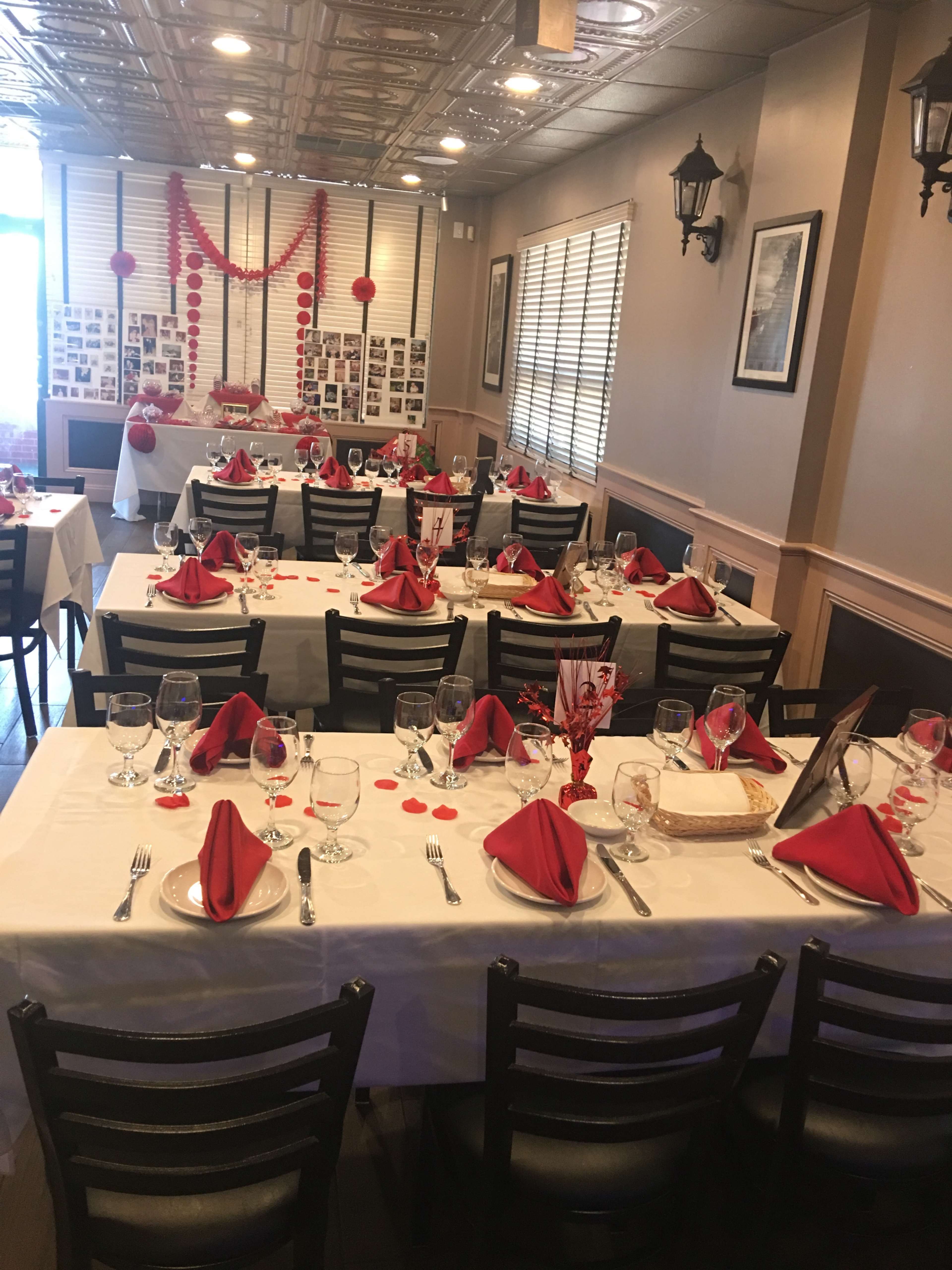The image shows a dining setup with several tables arranged with white tablecloths, red napkins, and decorative accents in a warmly lit restaurant.