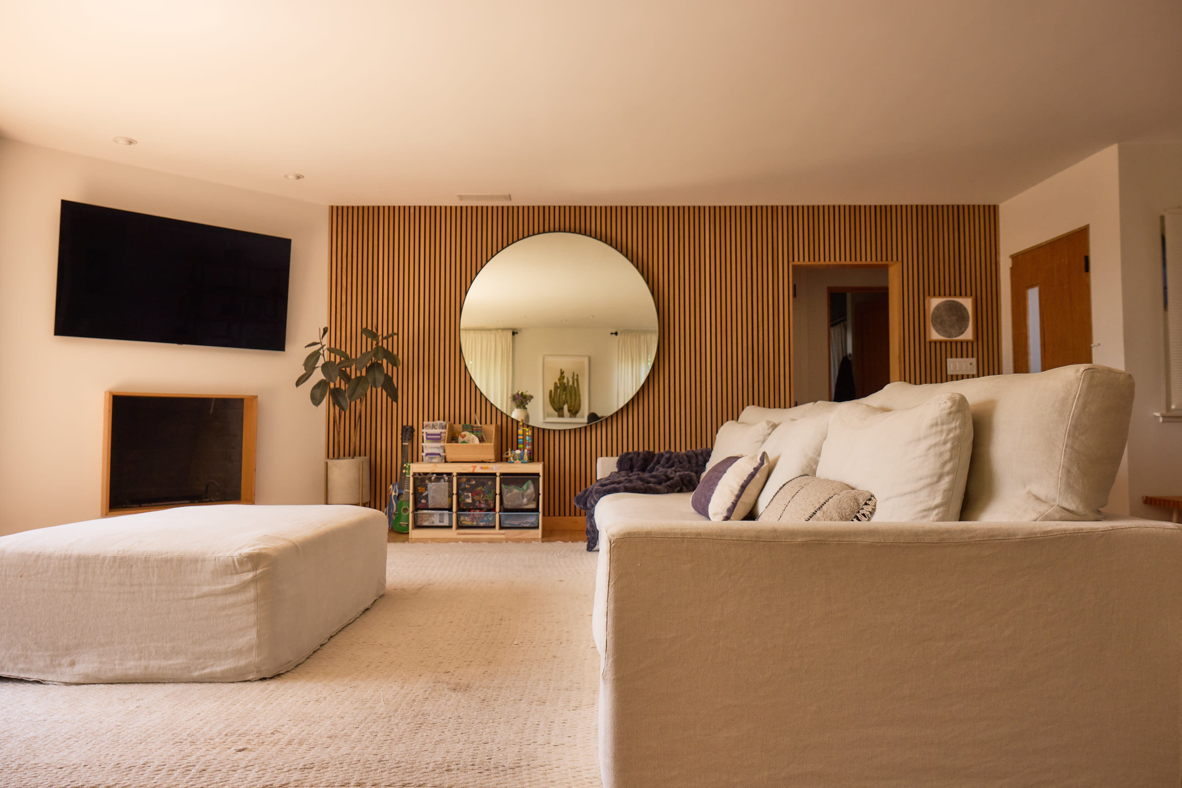 The image shows a modern living room featuring a large circular mirror, a sectional sofa, a coffee table, and a television mounted on the wall.