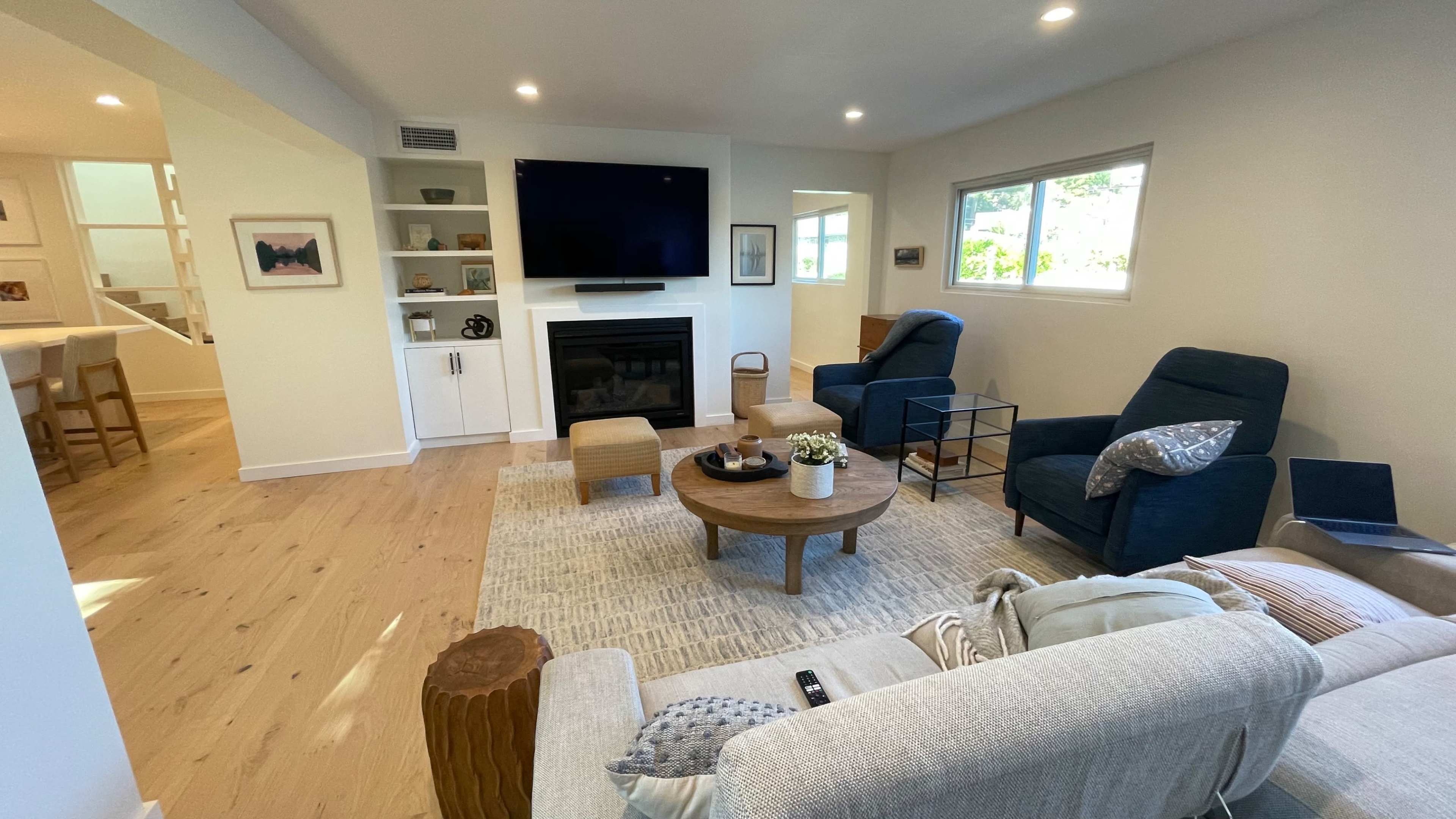 A modern living room with a fireplace, two blue chairs, a coffee table, and a TV mounted on the wall.