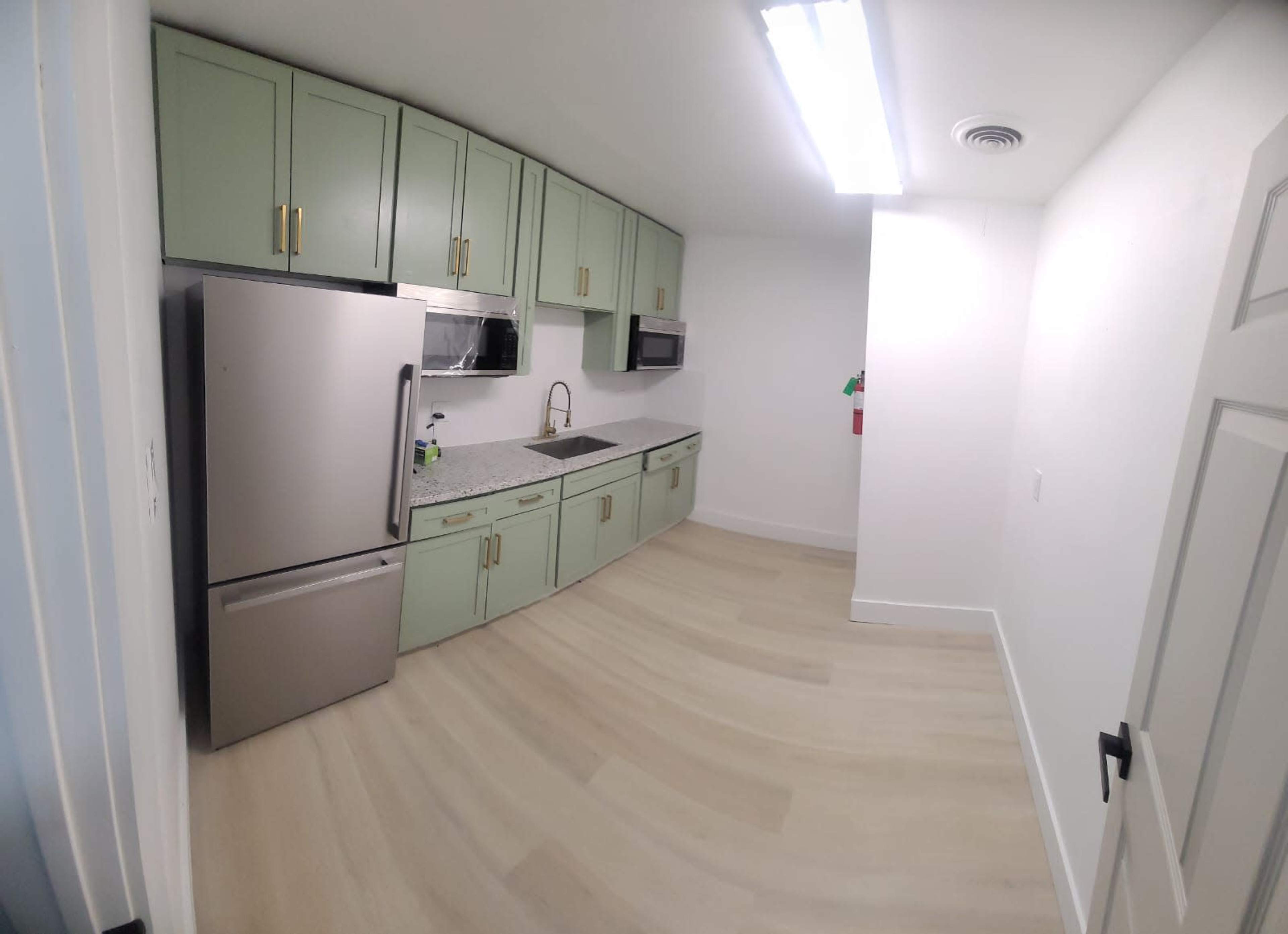 A modern kitchen with light green cabinets, stainless steel appliances, and a countertop with a sink.