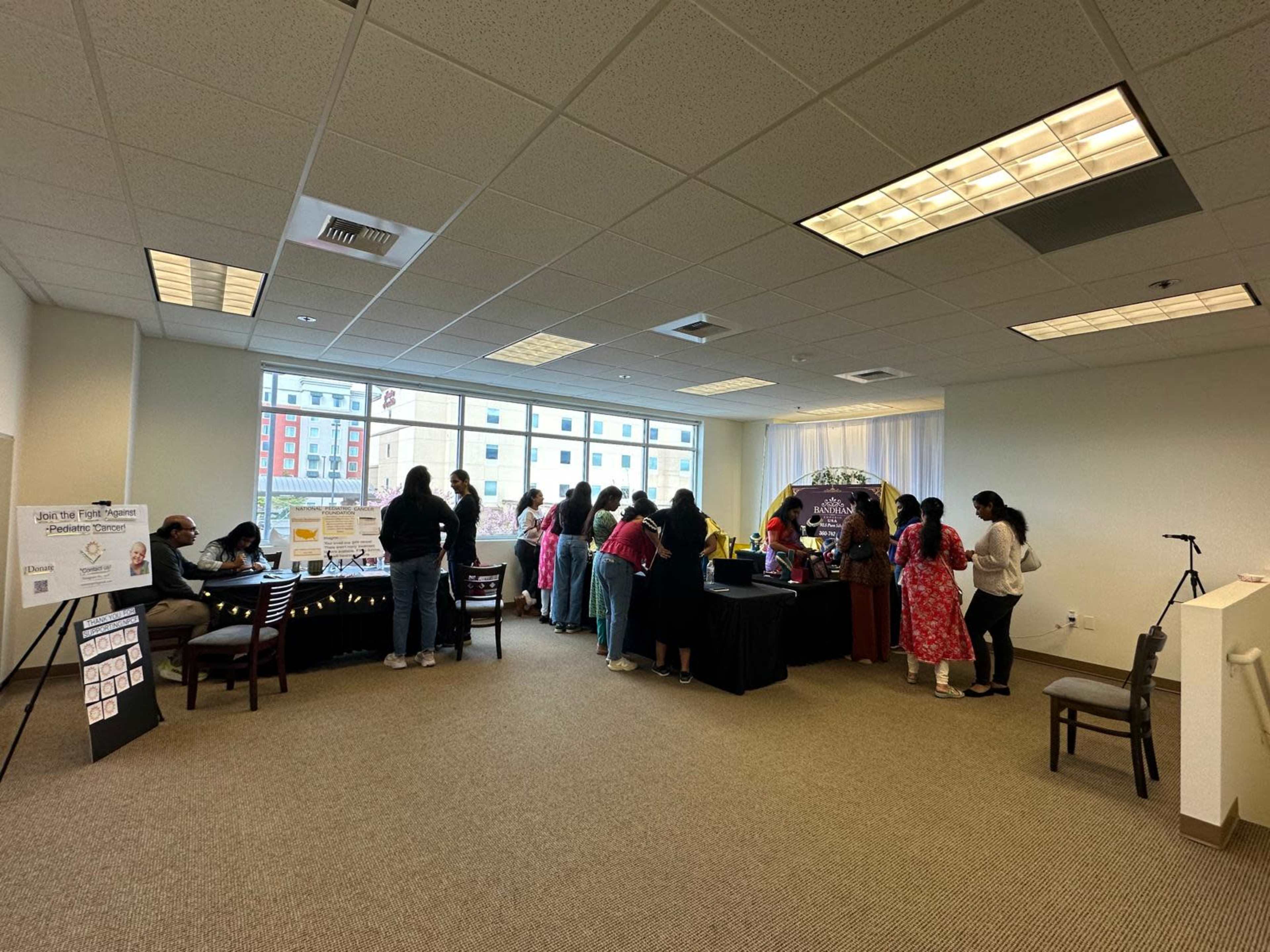 The image shows a community event taking place in a well-lit room with several tables set up, where attendees are engaging in various activities.