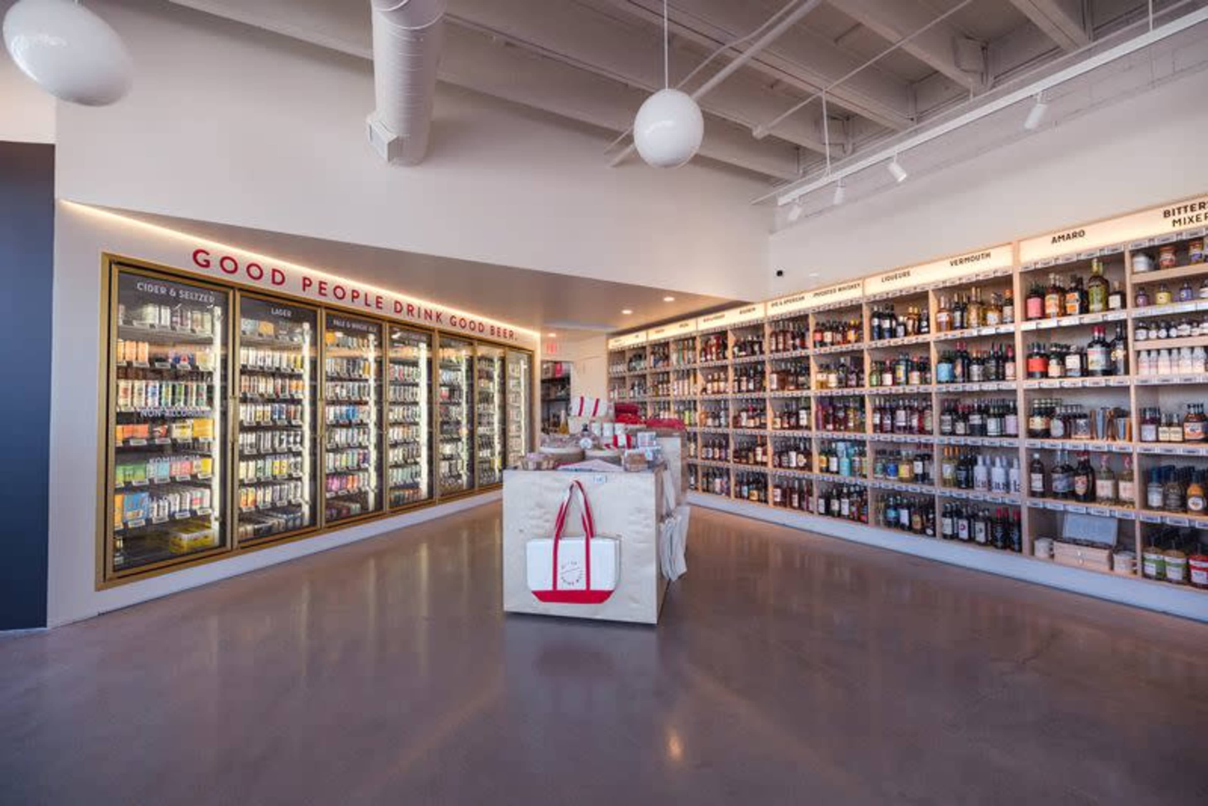 The image shows a well-organized beverage store with shelves lined with various drinks and a central display area featuring promotional items.