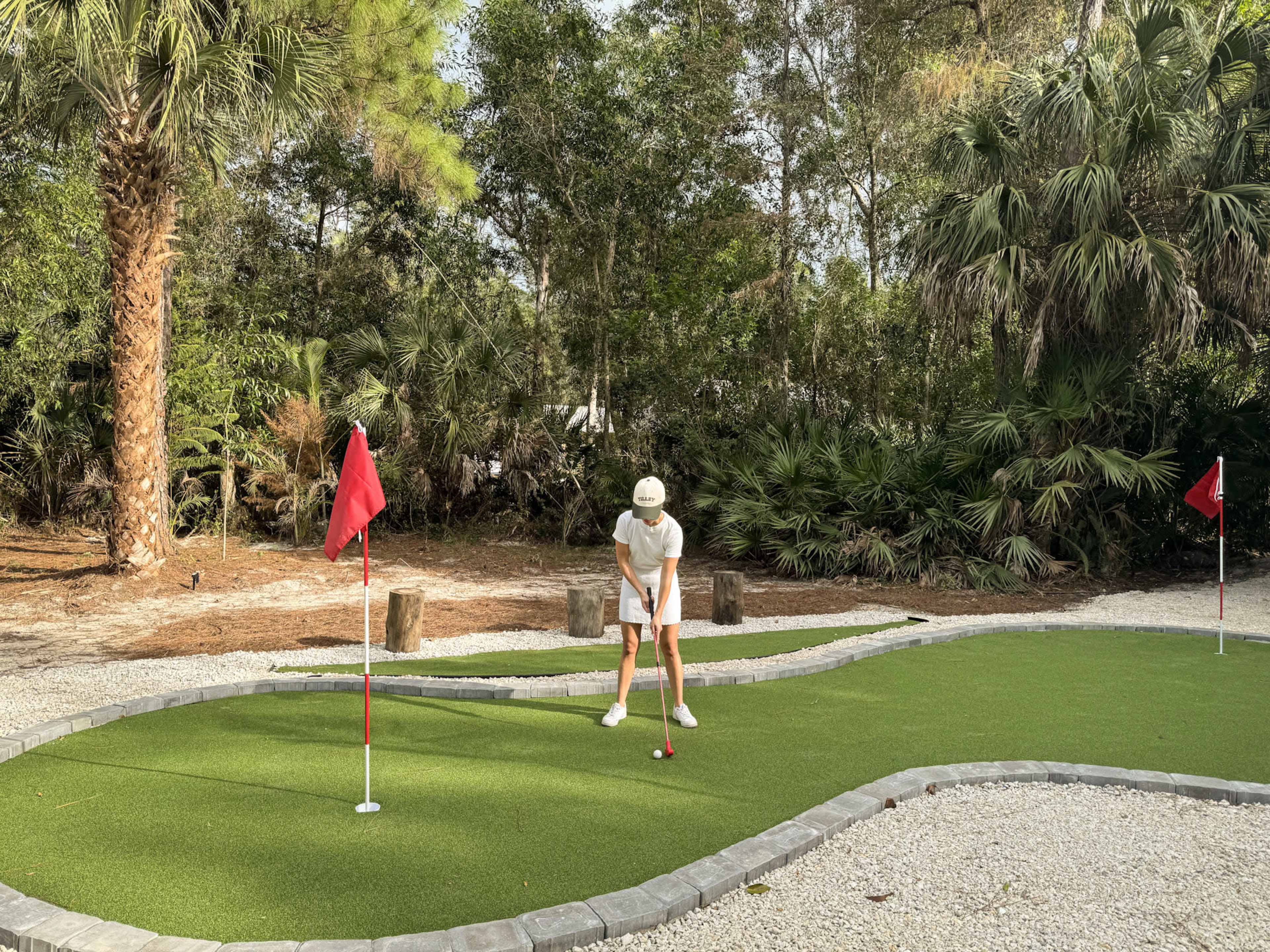 A person is putting on a mini-golf course surrounded by trees and shrubs.