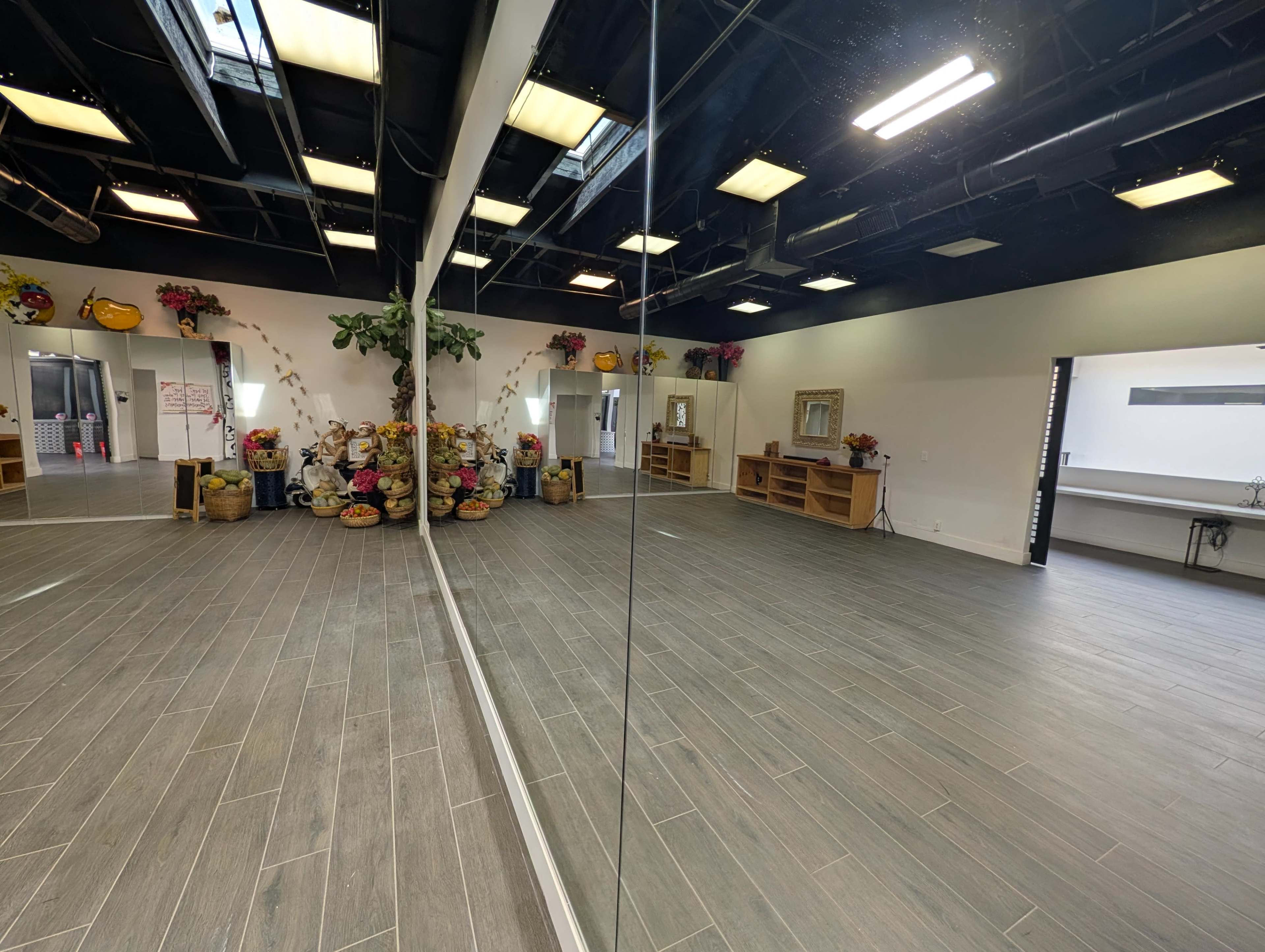 The image shows a spacious interior room with mirrored walls, wooden flooring, and colorful decorations featuring flowers and baskets.