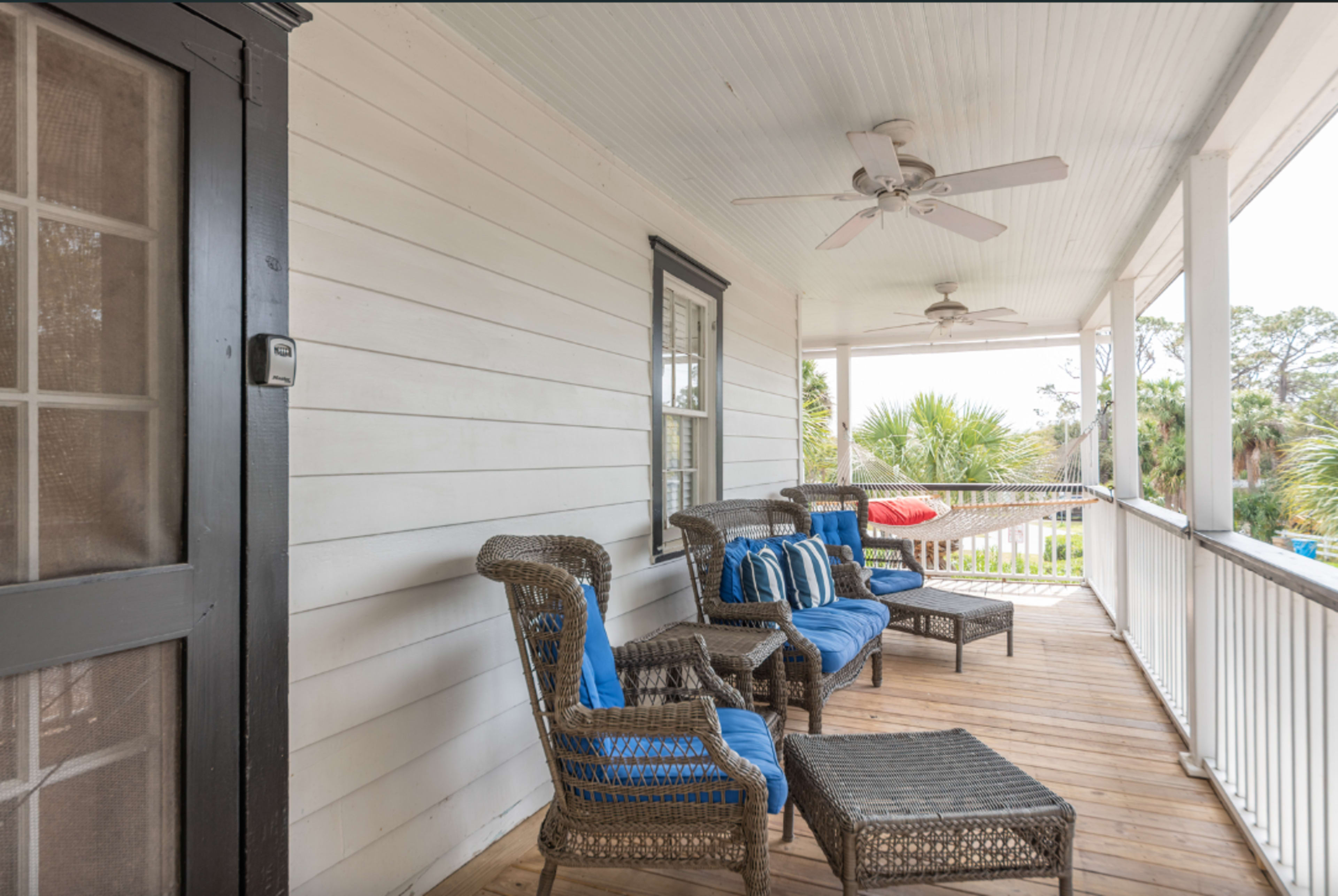 A porch with wicker seating, blue cushions, and a ceiling fan, surrounded by palm trees in the background.