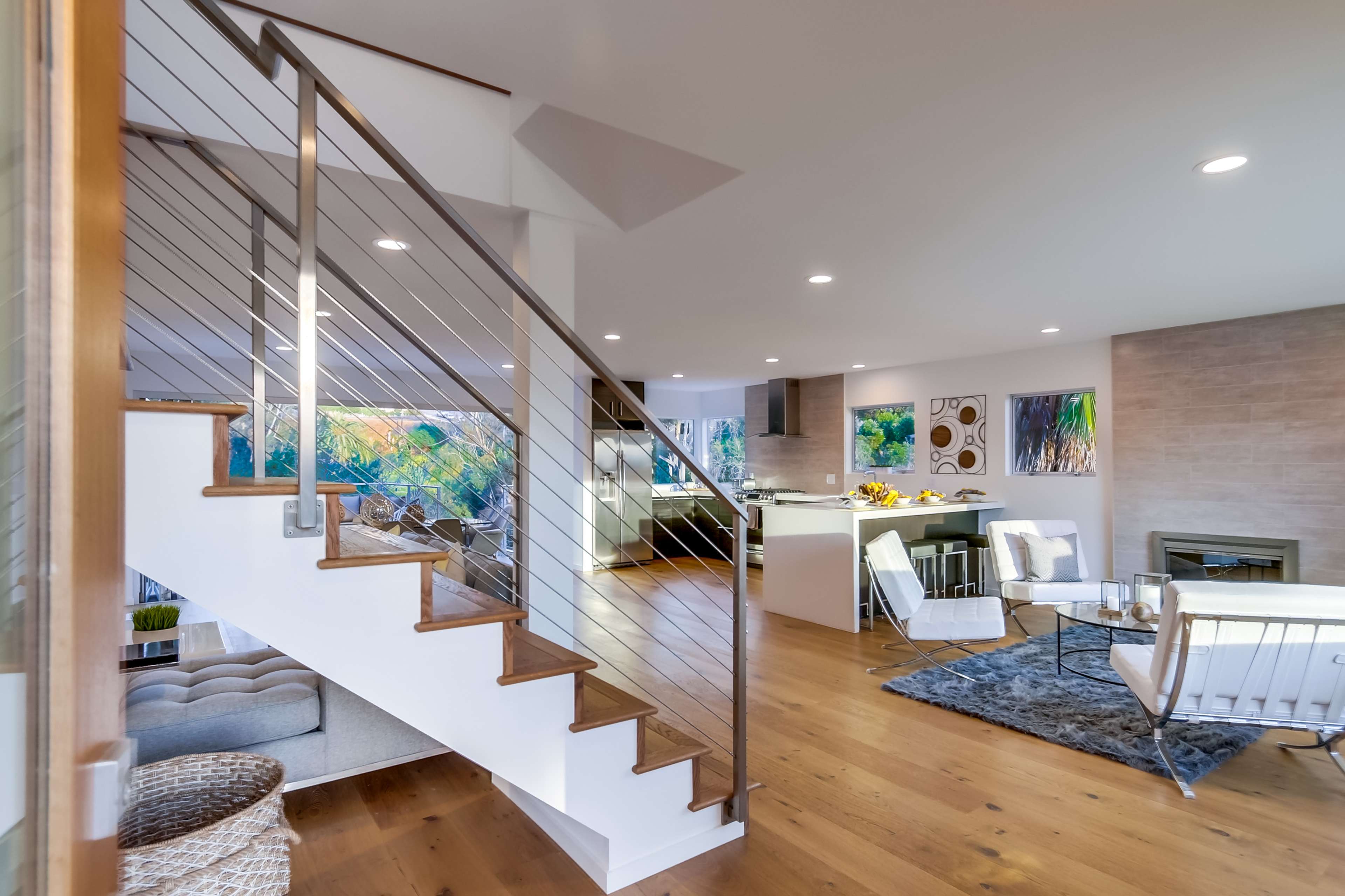 The image shows a modern interior space featuring a staircase with metal railings leading to a living area with a kitchen and seating.