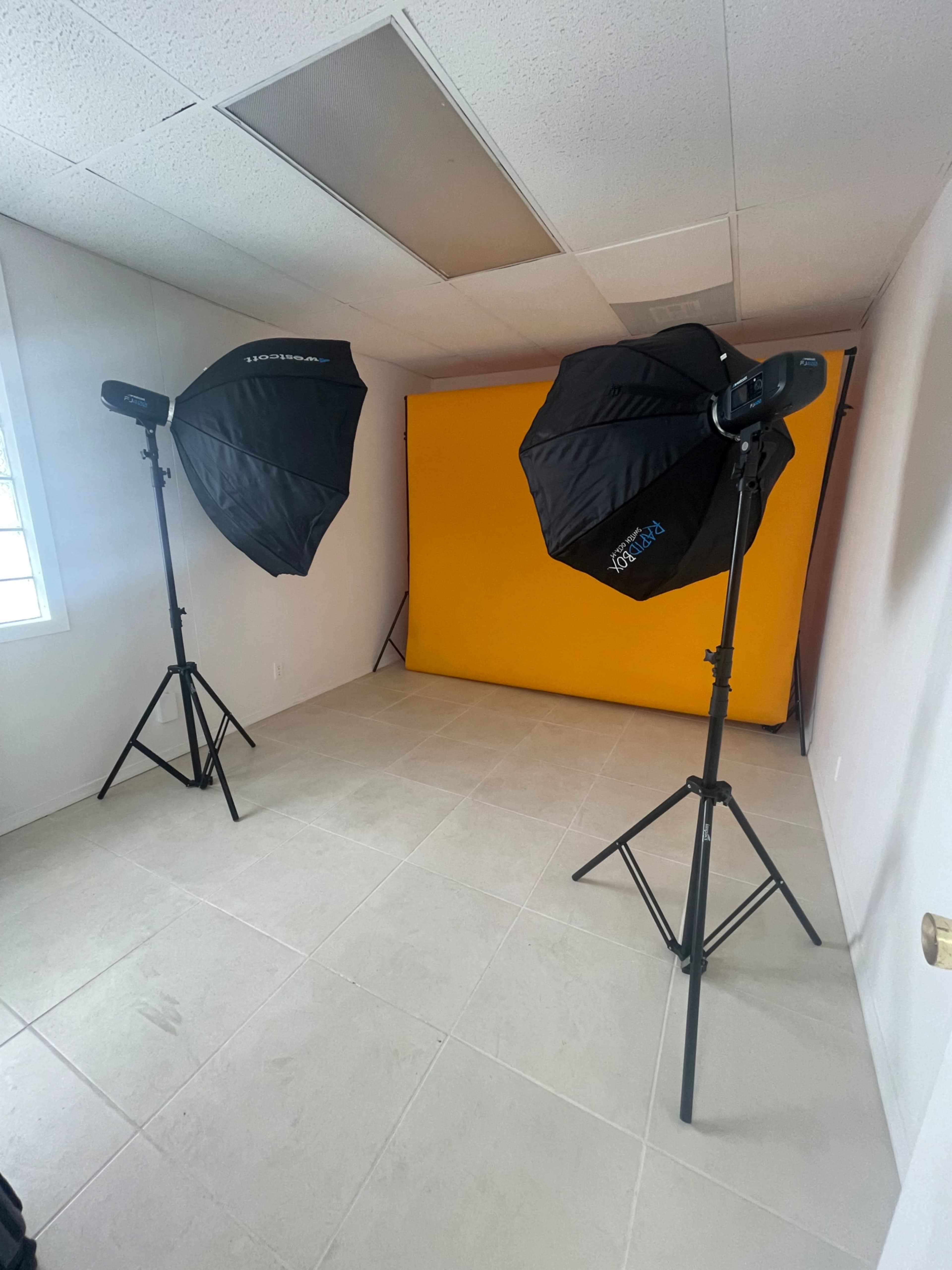 A well-lit photography studio with two softbox lights positioned on tripods facing a yellow backdrop.