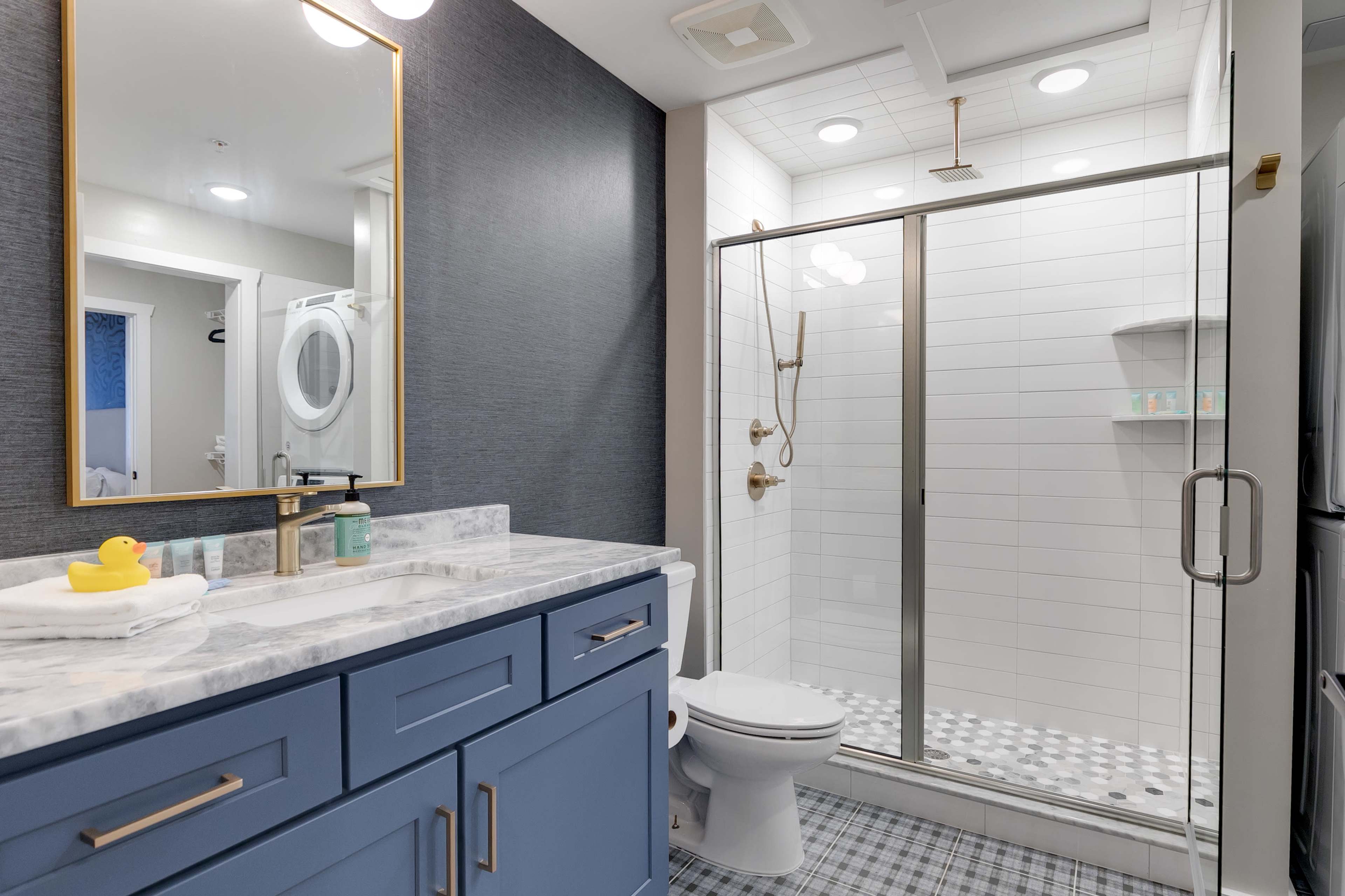A modern bathroom featuring a blue vanity with a marble countertop, a glass shower enclosure, and a toilet, all set against a textured wall and tiled flooring.