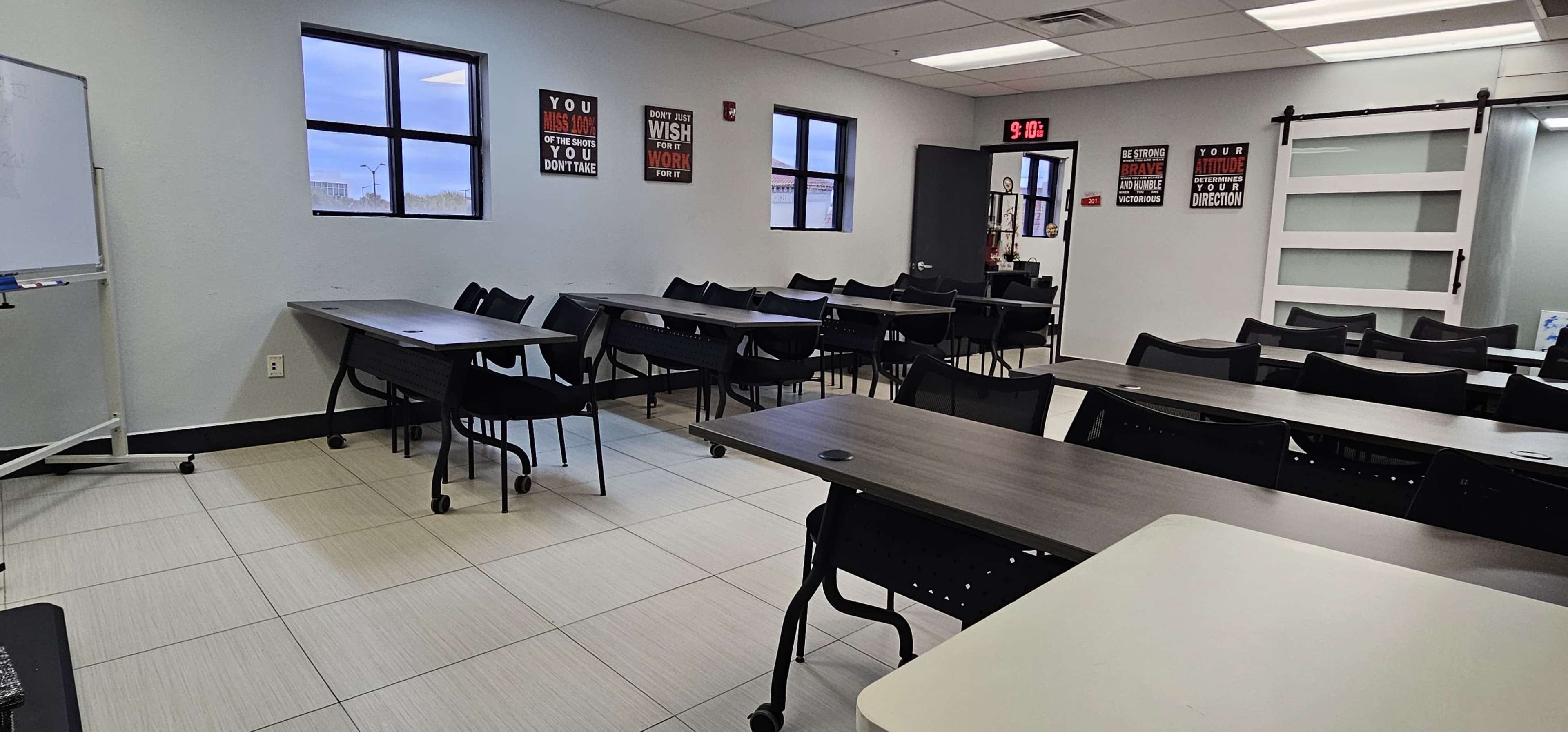 The image shows a classroom setting with several tables and chairs arranged in rows, along with motivational posters on the walls.