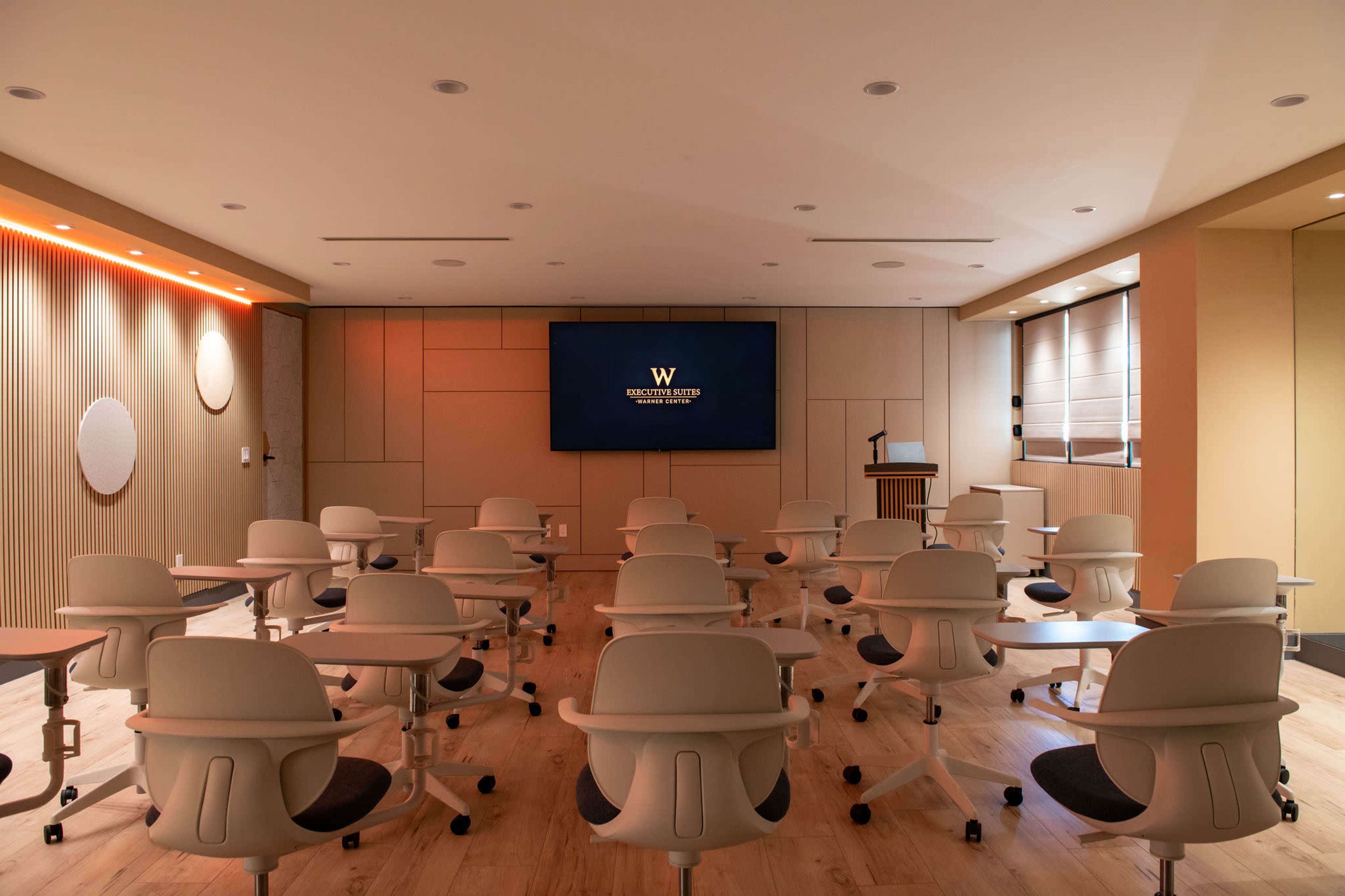 The image shows a modern classroom setup with multiple rows of movable chairs facing a large screen, emphasizing a professional learning environment.