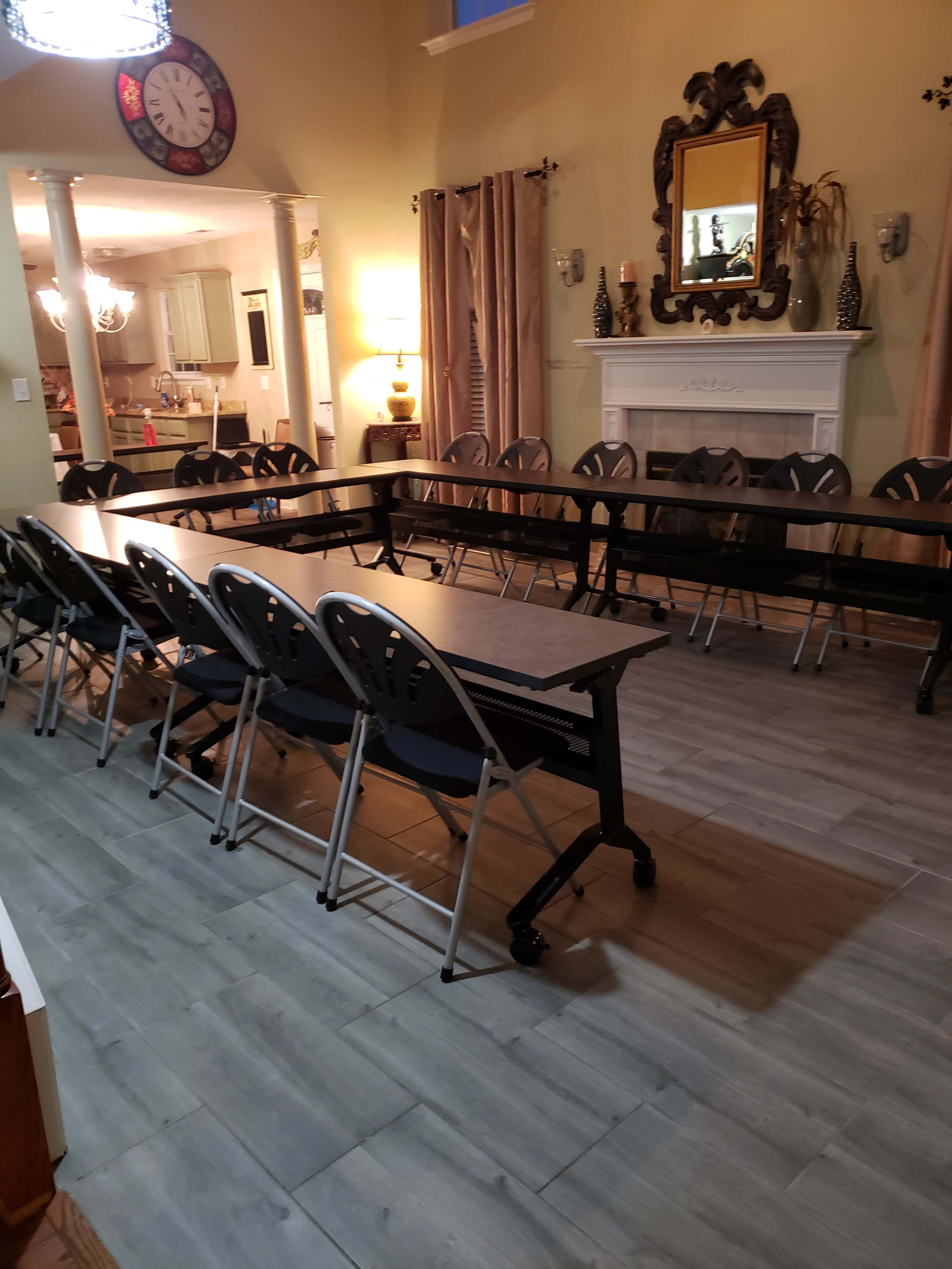 A long table with folding chairs is set up in a spacious room that features a fireplace and decorative wall mirrors.
