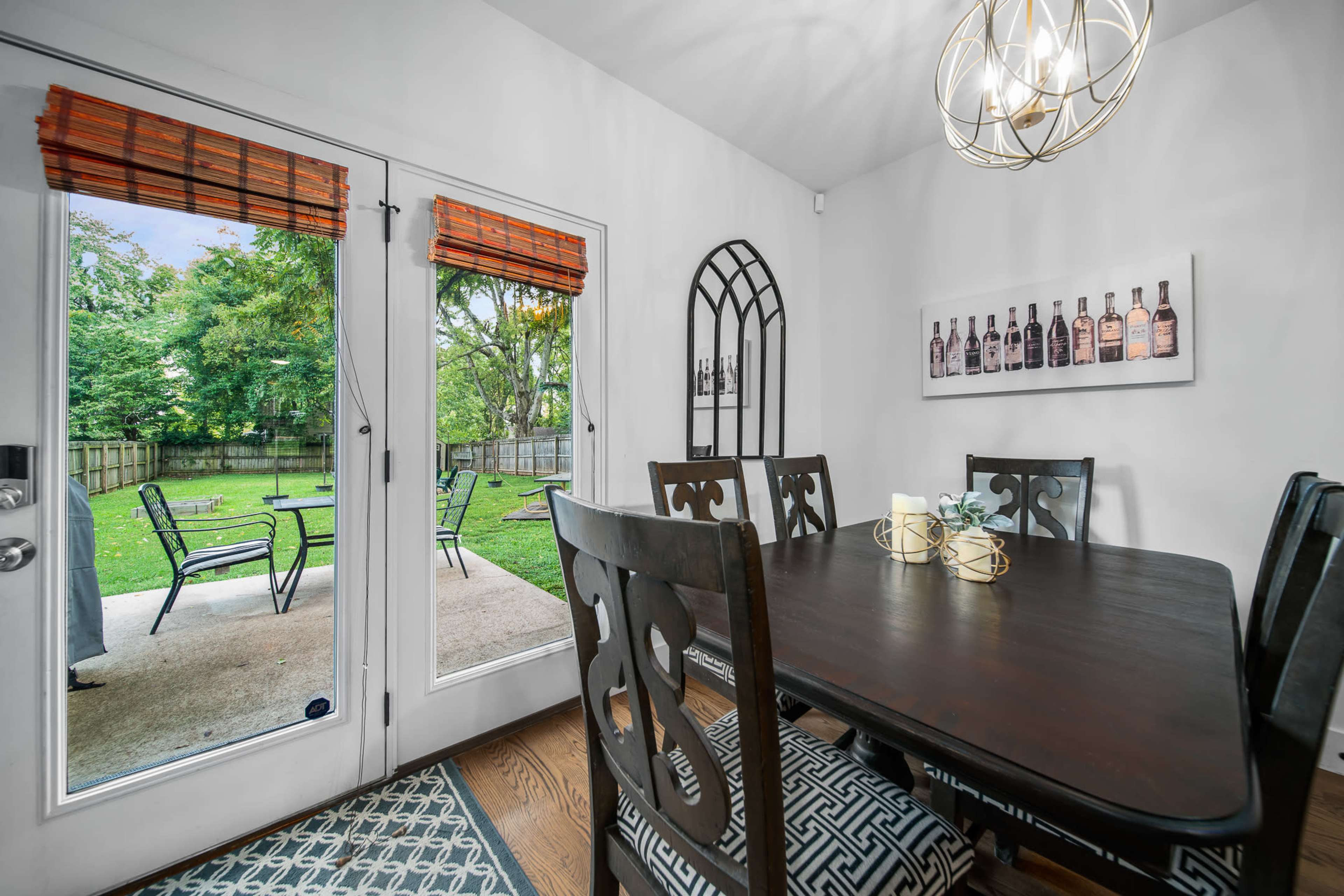 A dining area features a dark wooden table surrounded by chairs, with glass doors that open to a backyard visible through the open entrance.