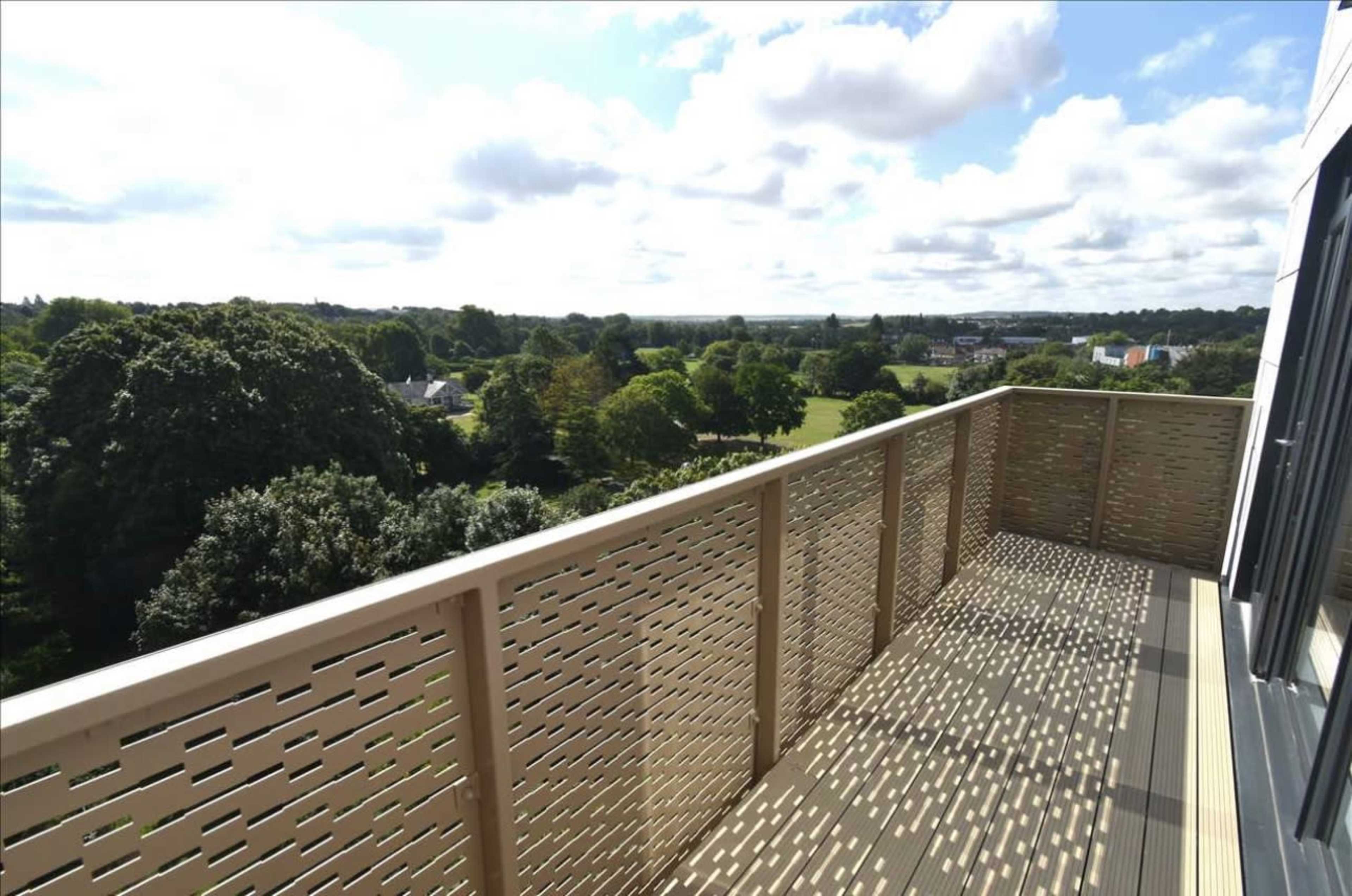 A balcony with a patterned railing overlooks lush greenery and a clear sky.