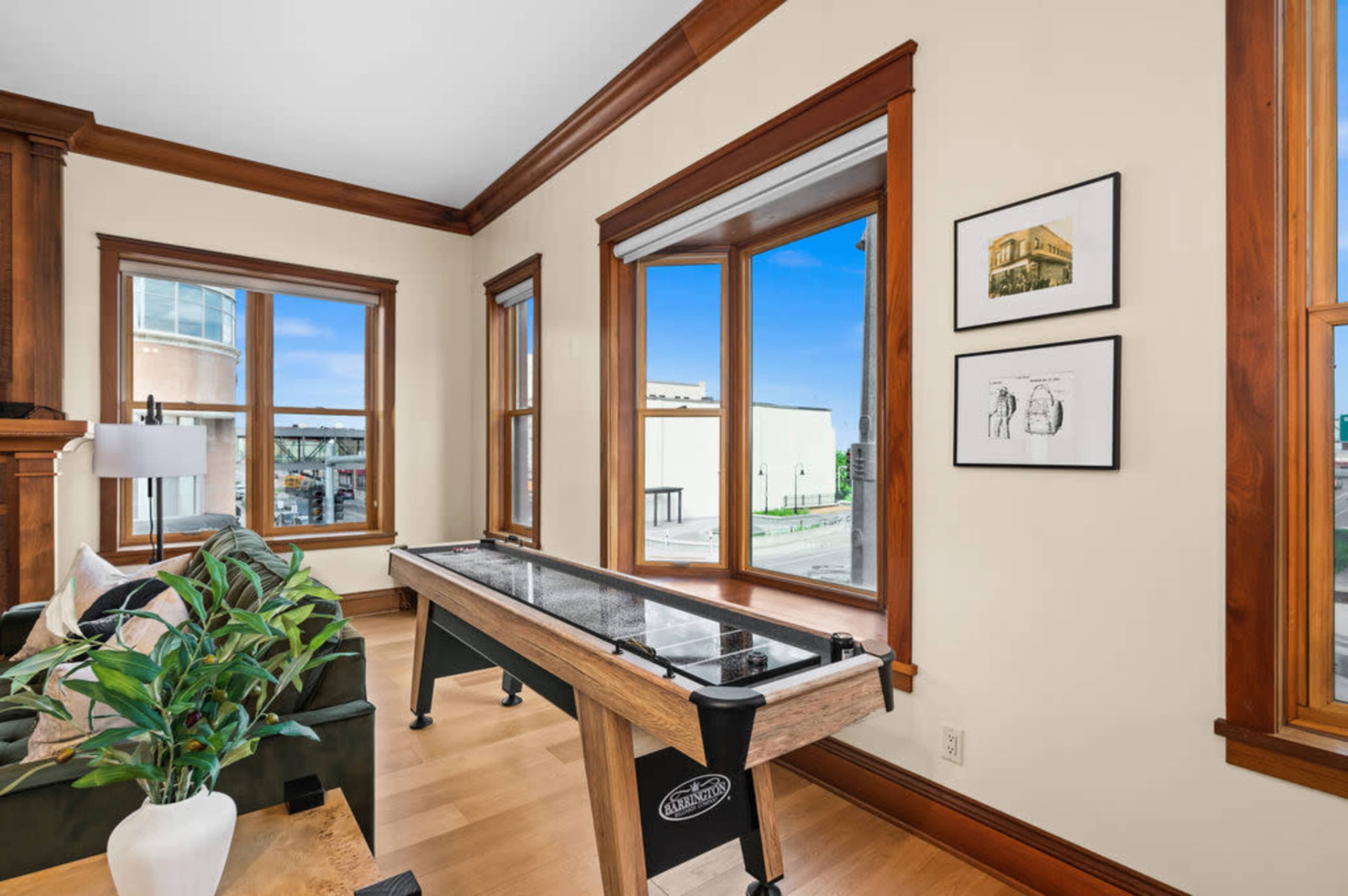 A room featuring a shuffleboard table, large windows with a view, and wooden trim along the walls.