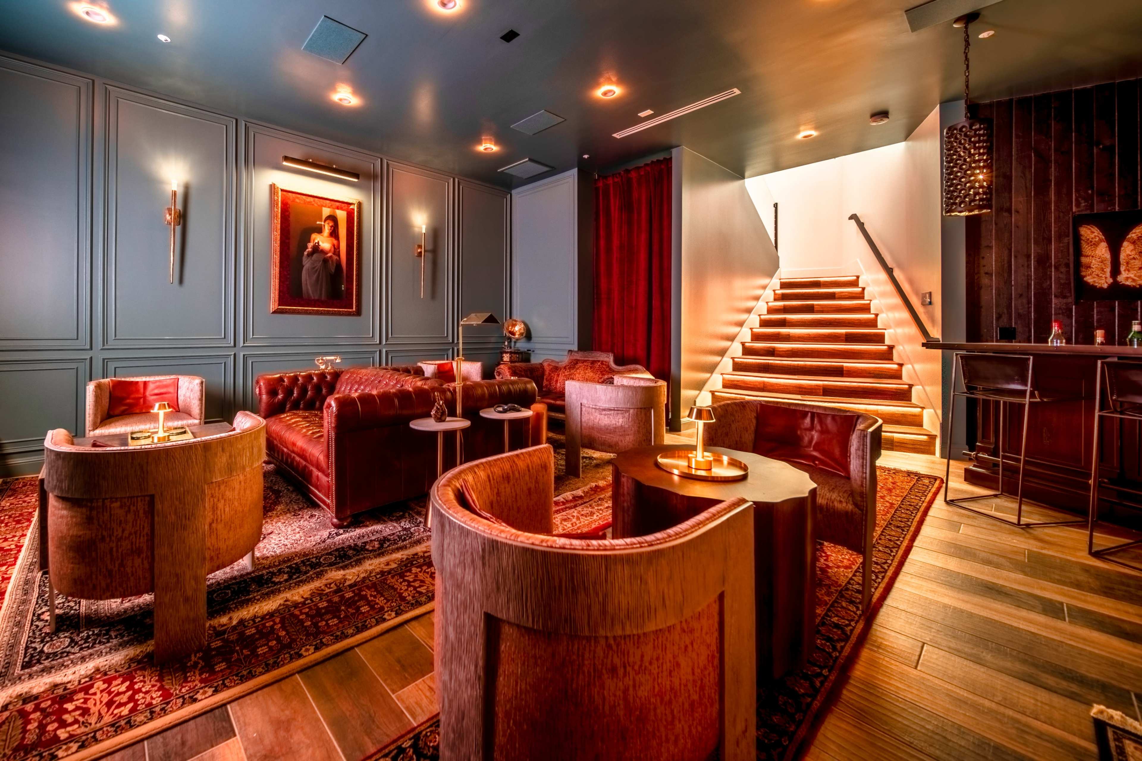 A stylish lounge area with leather seating, decorative artwork on the walls, and a staircase leading to a different level.