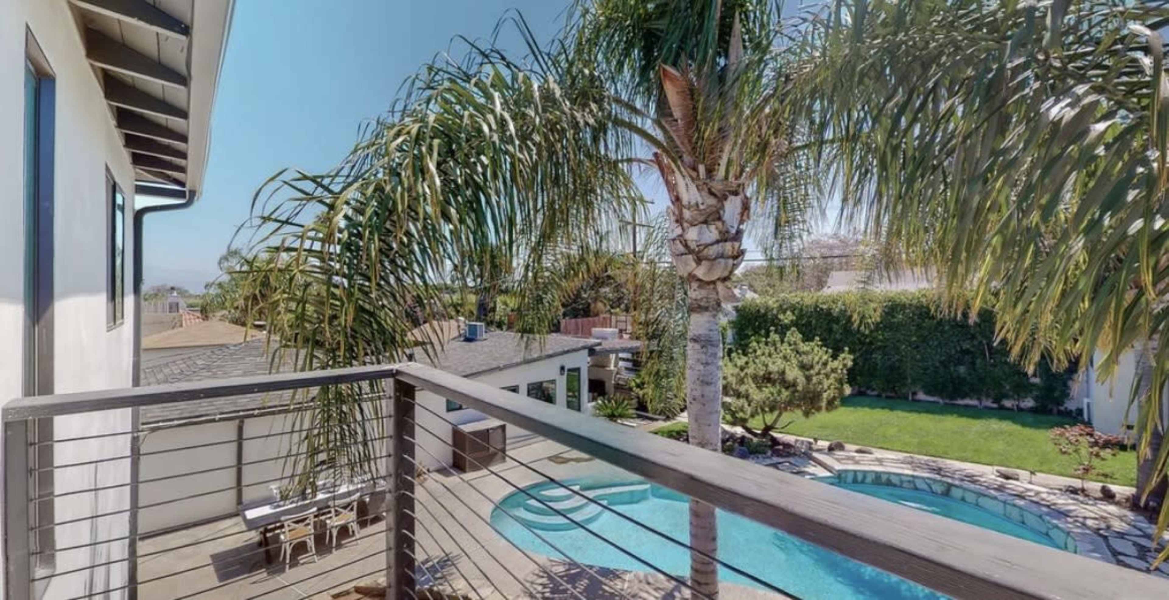 The image shows a balcony view overlooking a pool surrounded by palm trees and landscaped gardens.