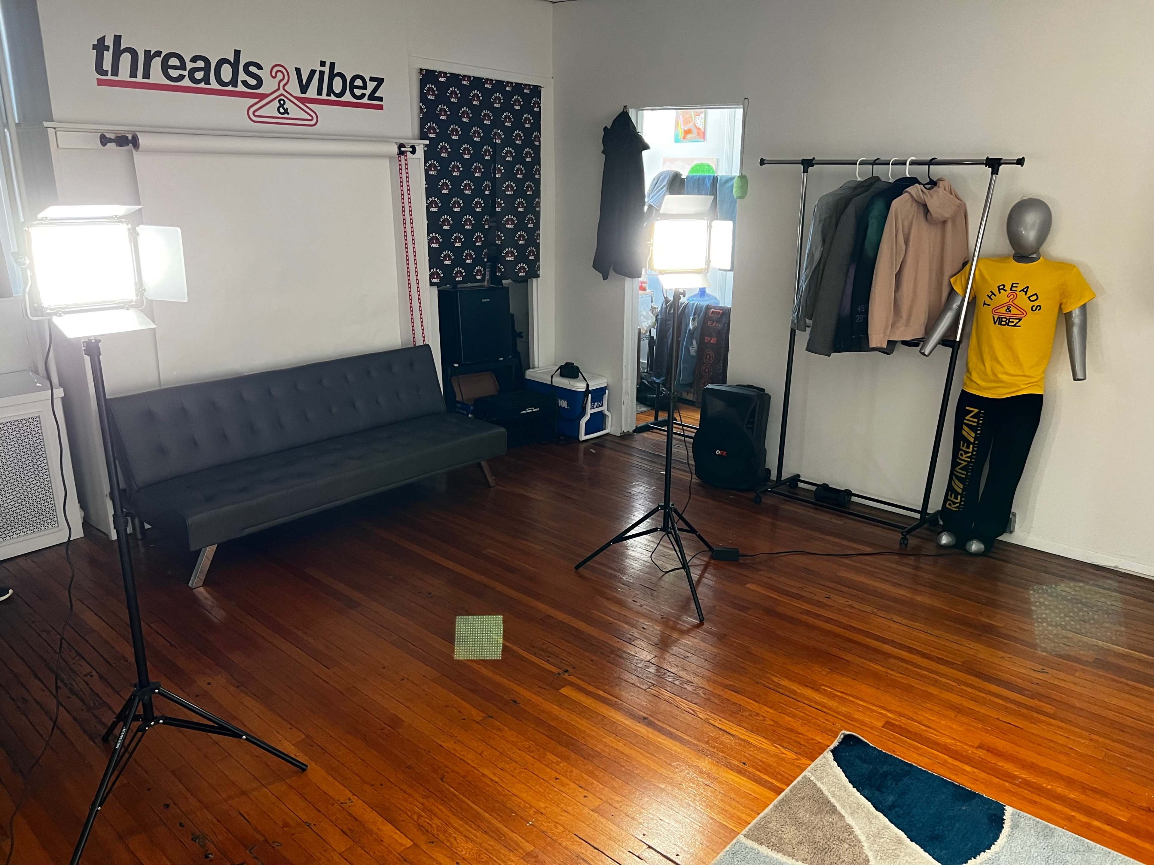 A small studio space with a gray sofa, clothing rack, and bright lighting equipment set up for a photoshoot or display.