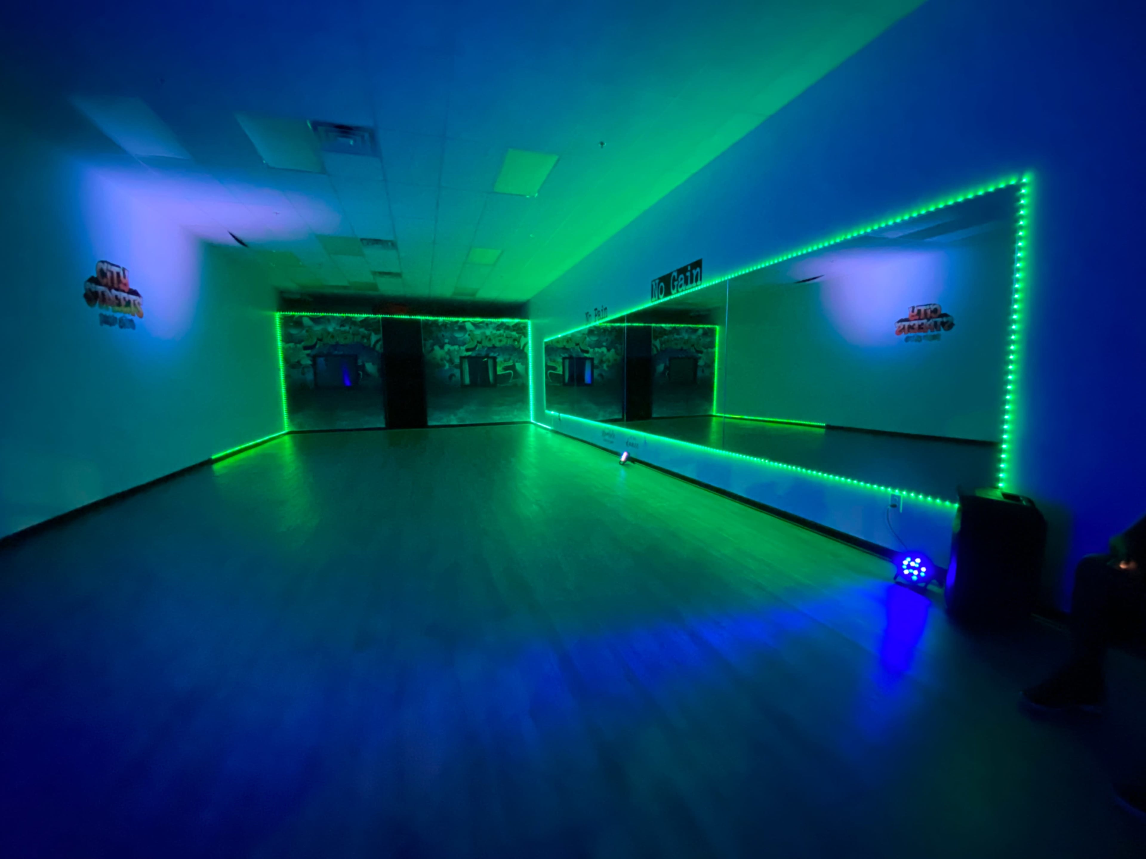A dance studio features mirrored walls illuminated with green and blue LED lights.