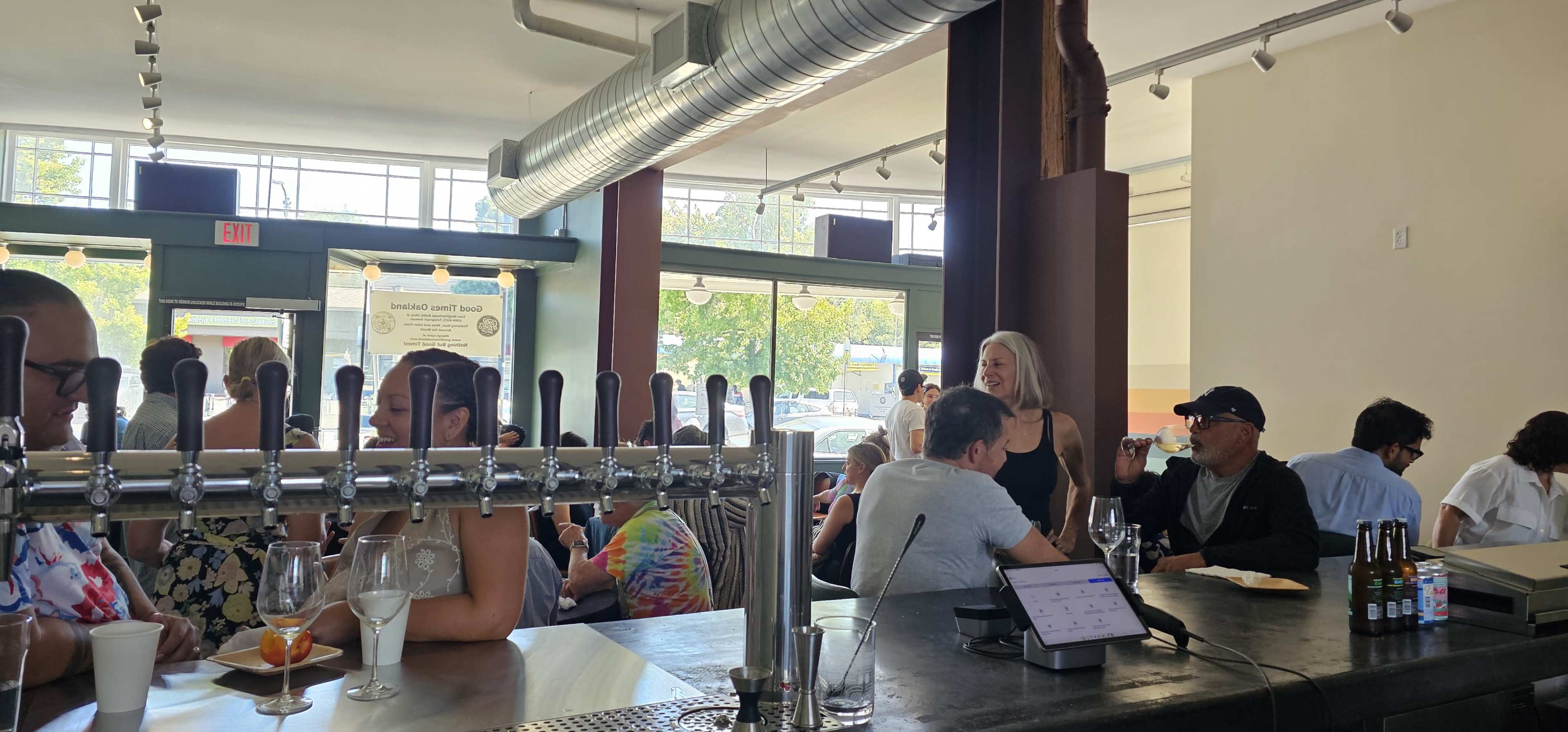The image shows a lively café scene with people chatting and enjoying drinks at a bar, while others sit at tables near large windows.