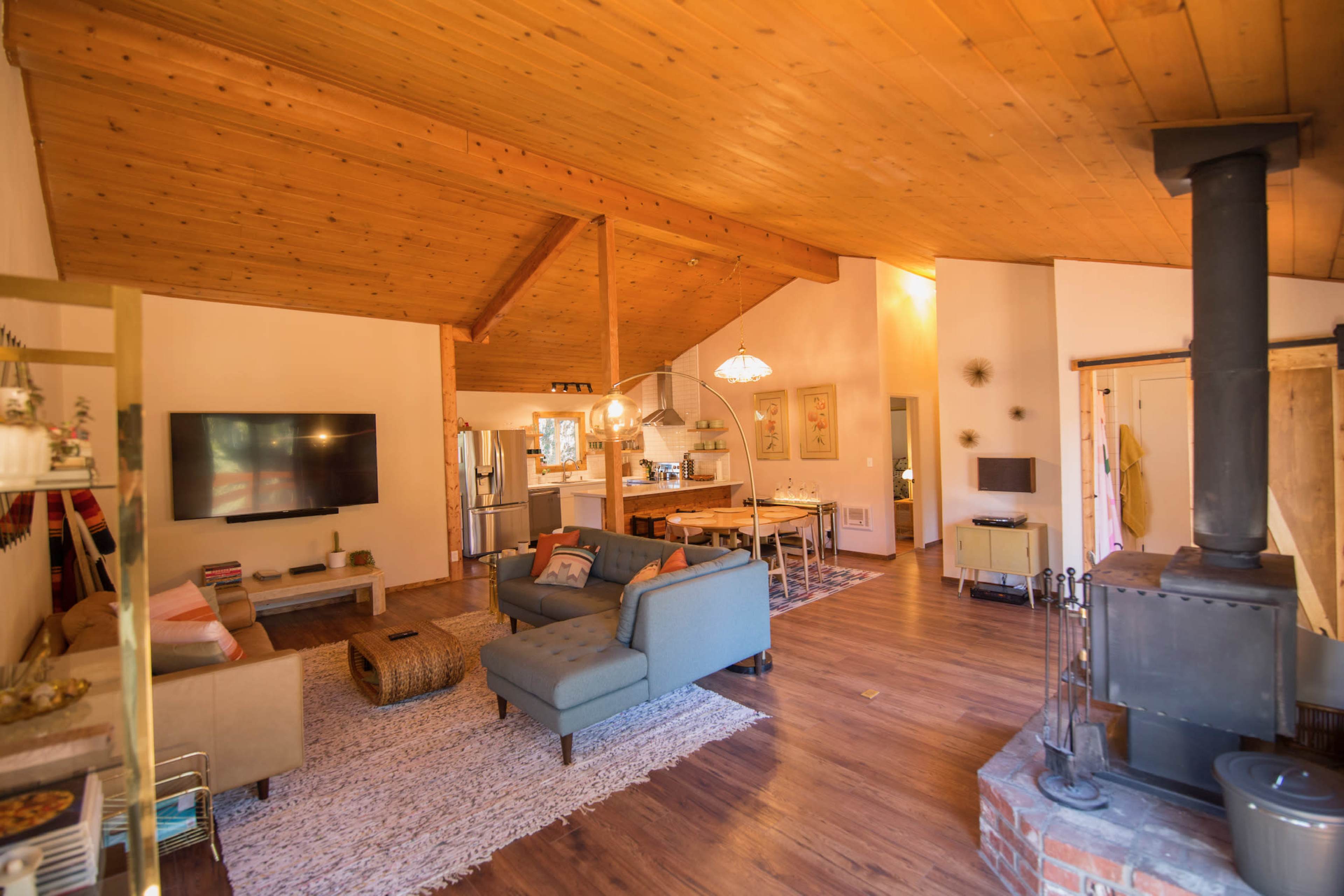 An open-concept living area with a wooden ceiling, two seating arrangements, a television, and a dining area in the background.