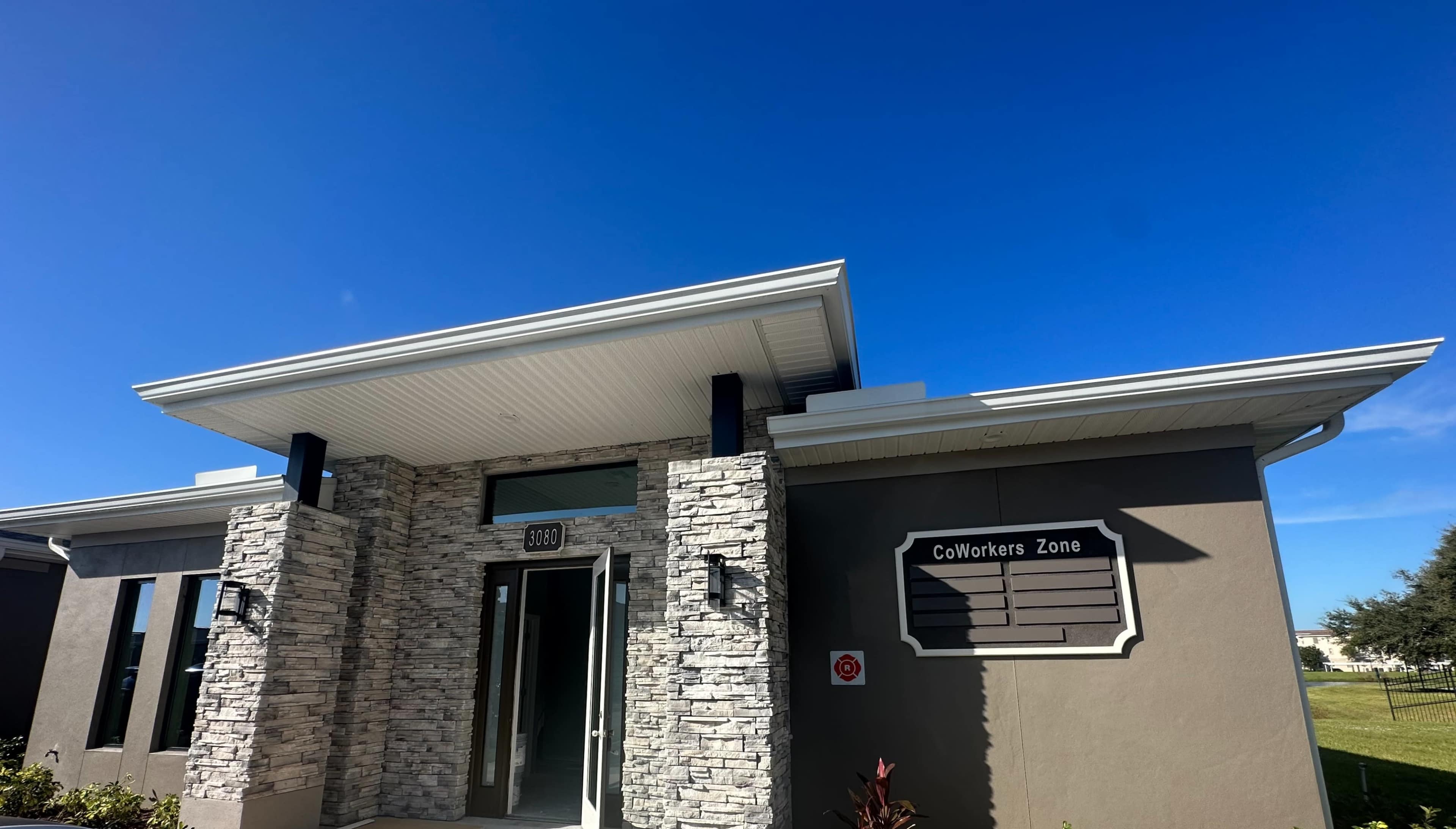 The image shows a modern building with stone accents and a sign that reads "CoWorkers Zone" on the side.