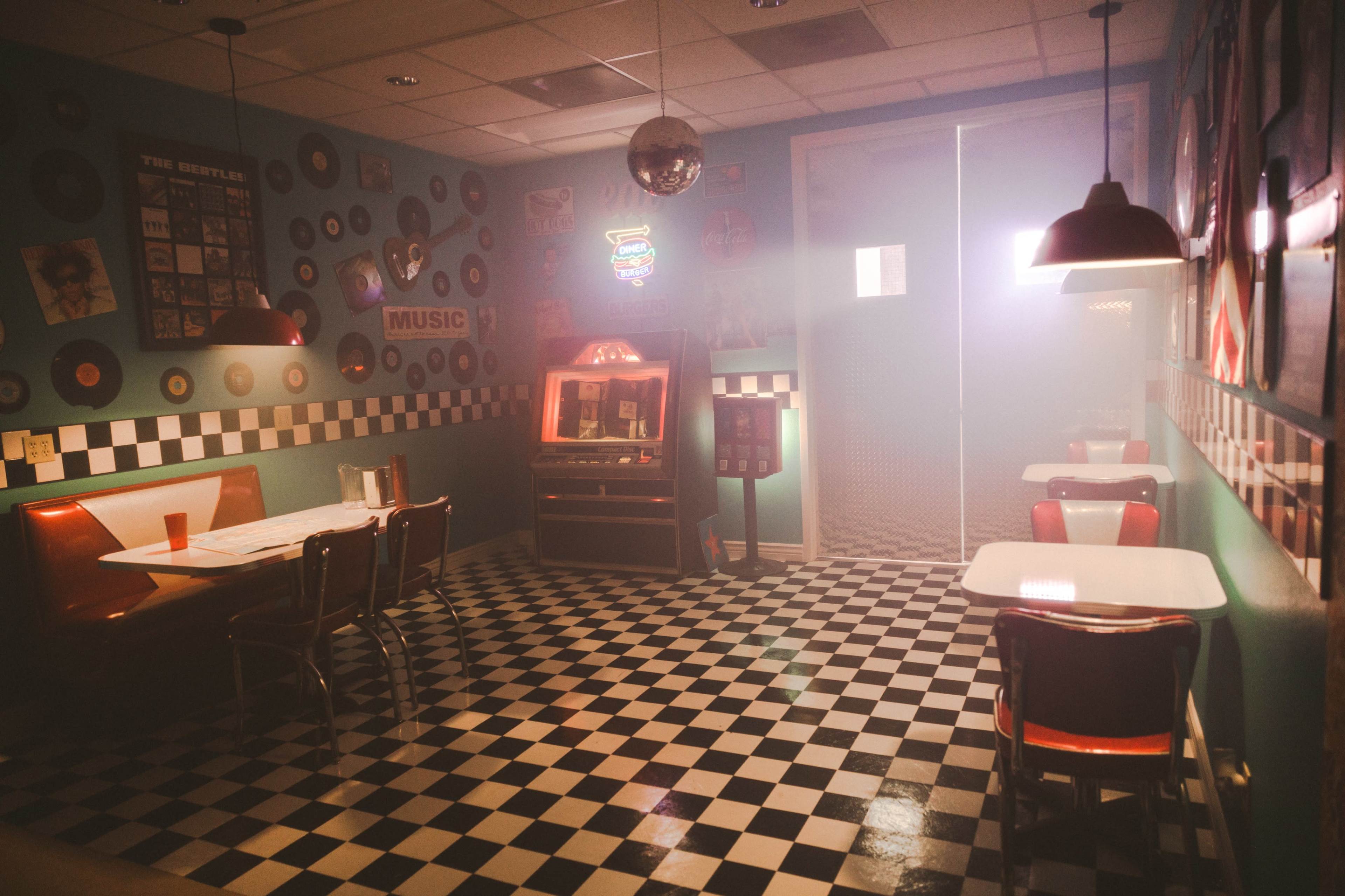 A retro diner features checkered flooring, red booths, a jukebox, and vinyl records decorating the walls, all shrouded in a misty ambiance.