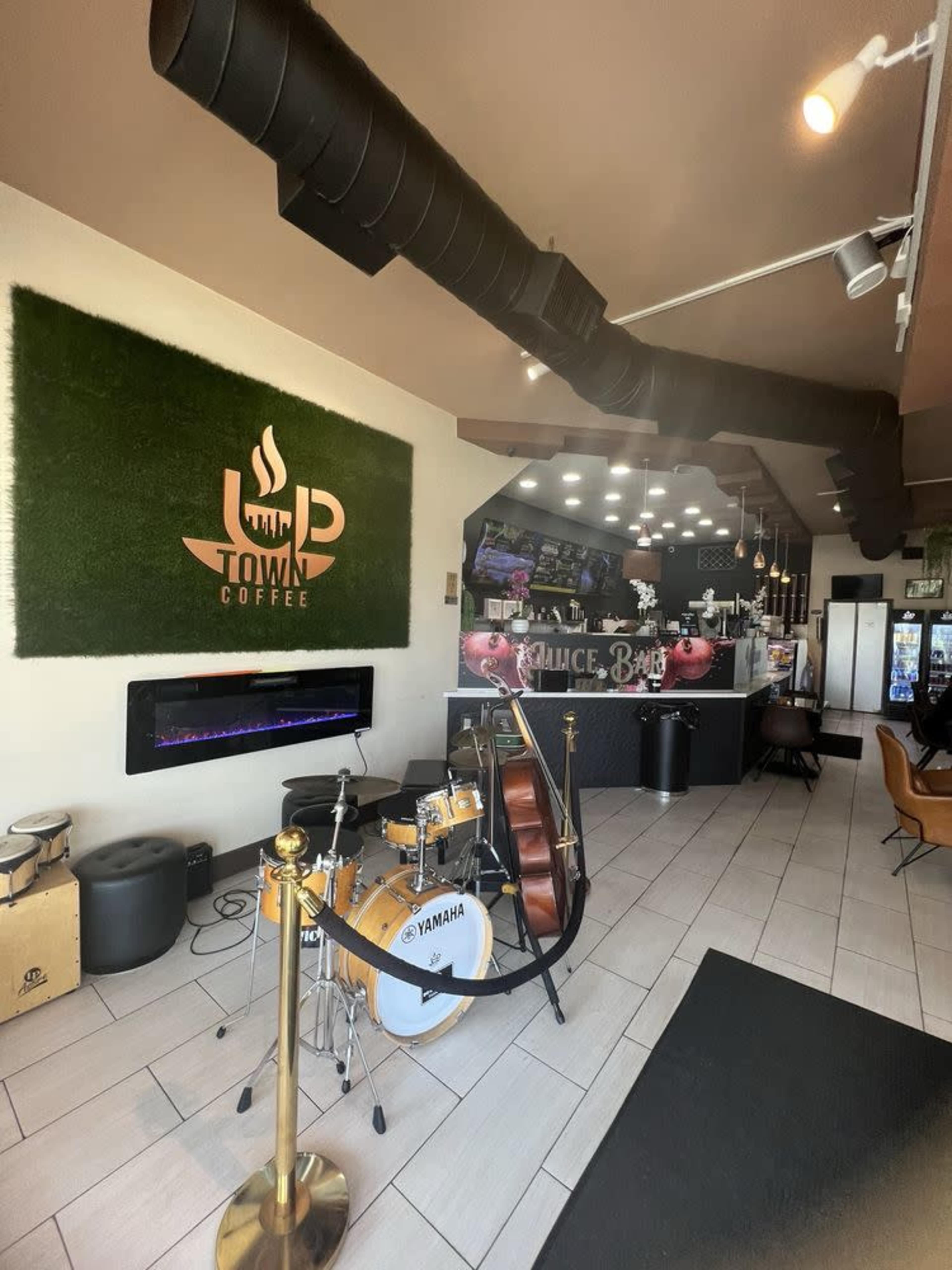 The image shows a coffee shop interior featuring a green wall with a logo, a music corner with a drum set and a double bass, and a service counter in the background.