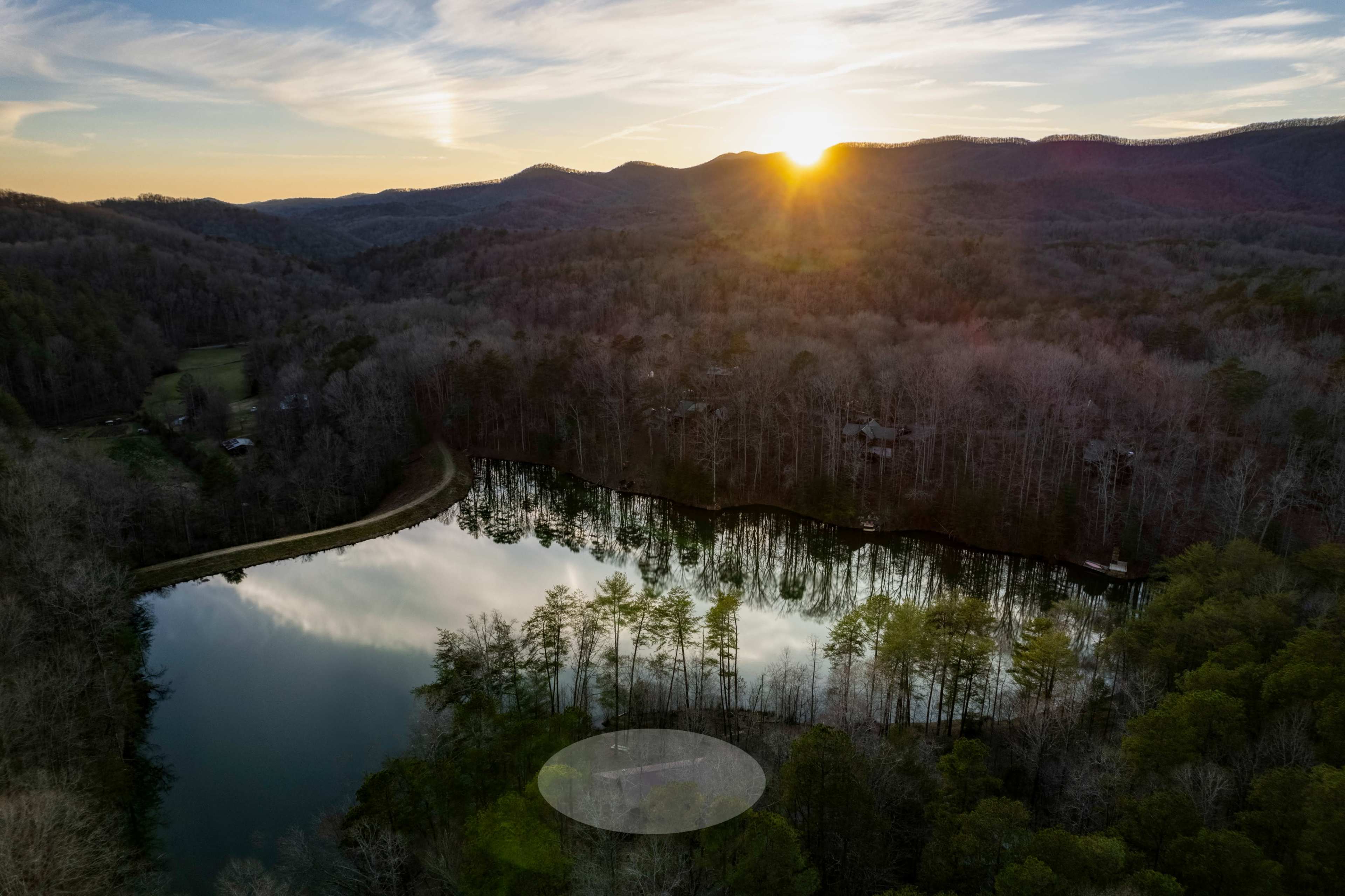 A serene landscape with a lake reflecting trees and a sunset, surrounded by rolling hills.