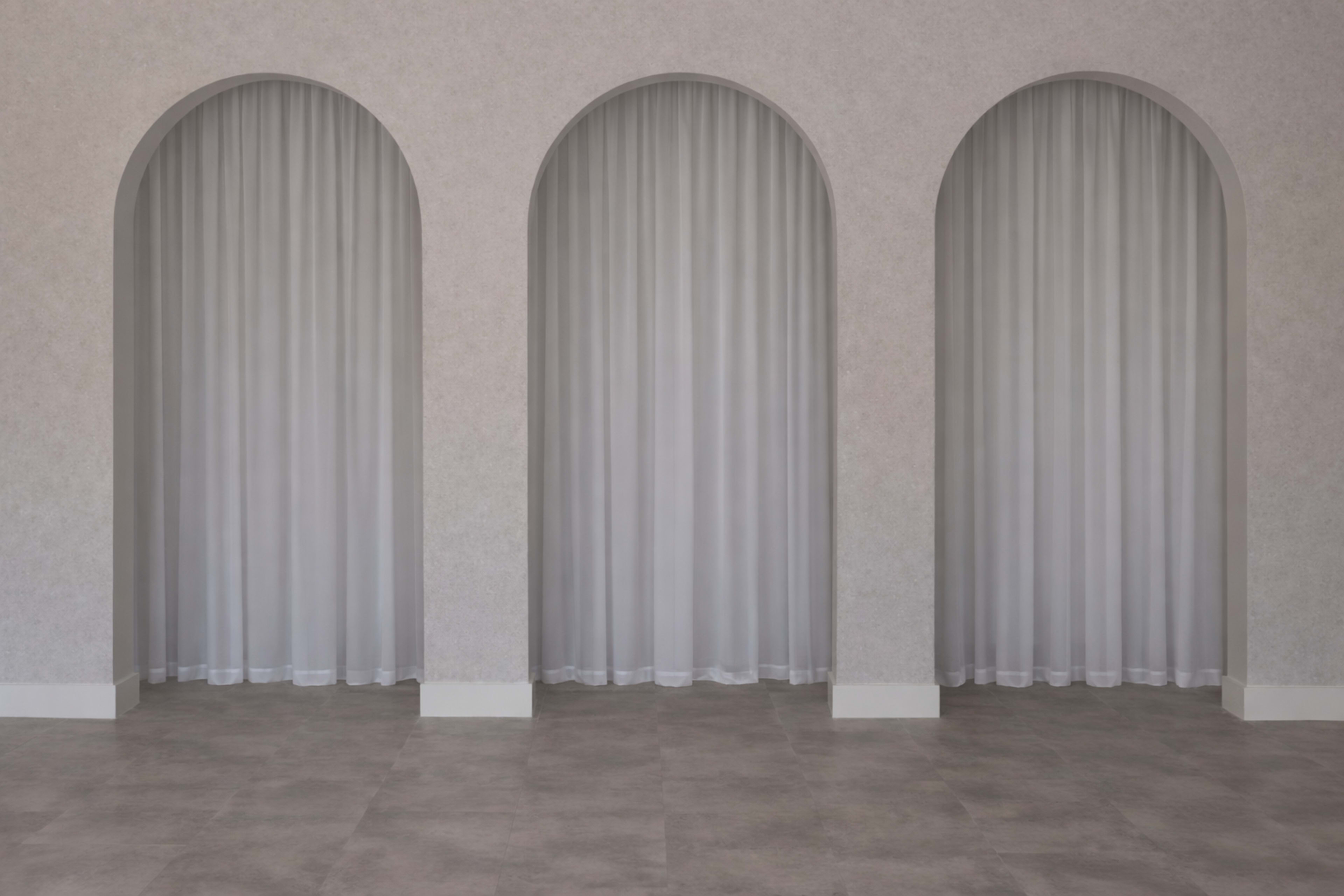 The image shows three arched openings in a textured wall, each adorned with sheer curtains and set on a tiled floor.
